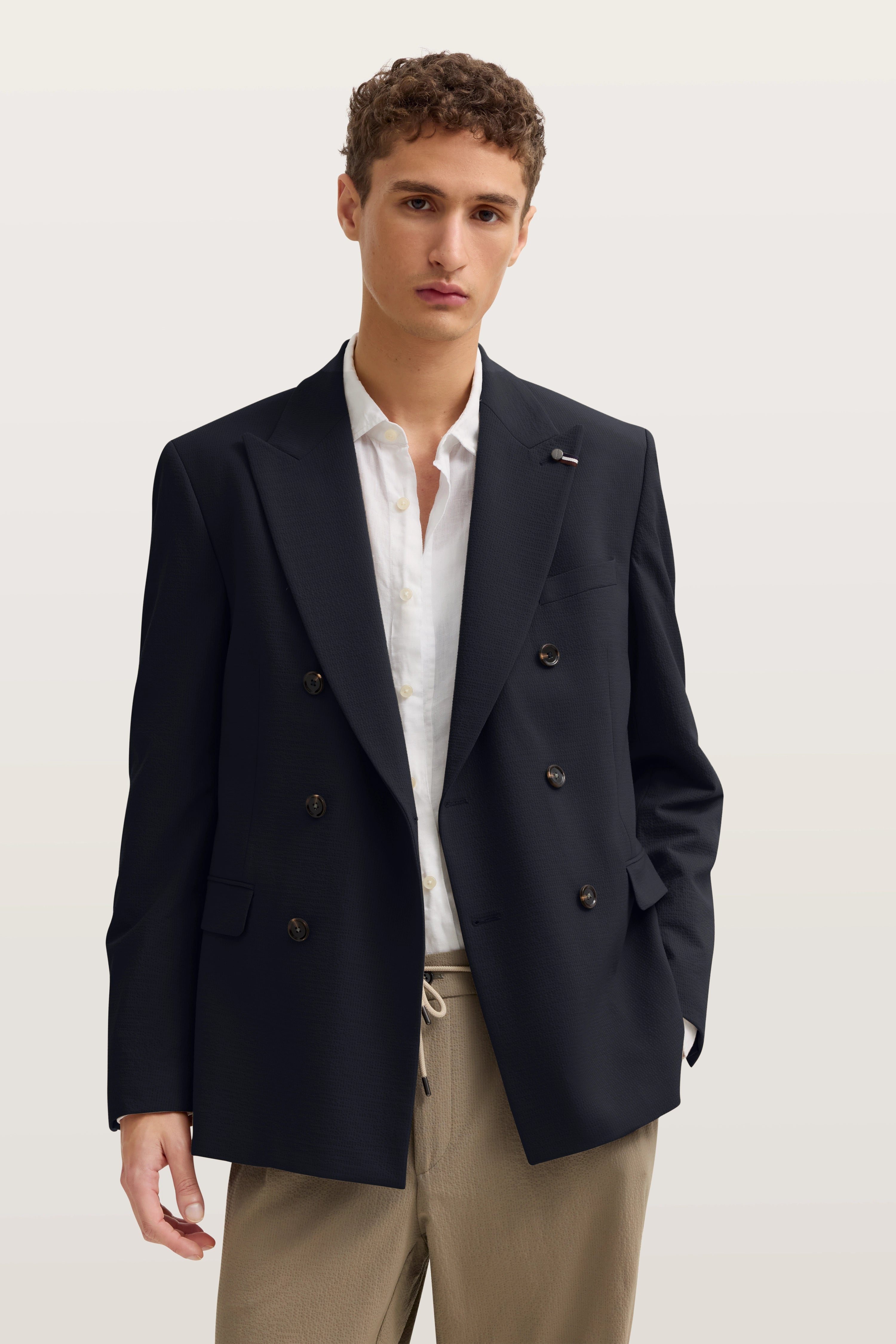 Bugatti Model in marineblauem Doppelreiher-Blazer, weißes Hemd, beige Hose, legeres Posing.