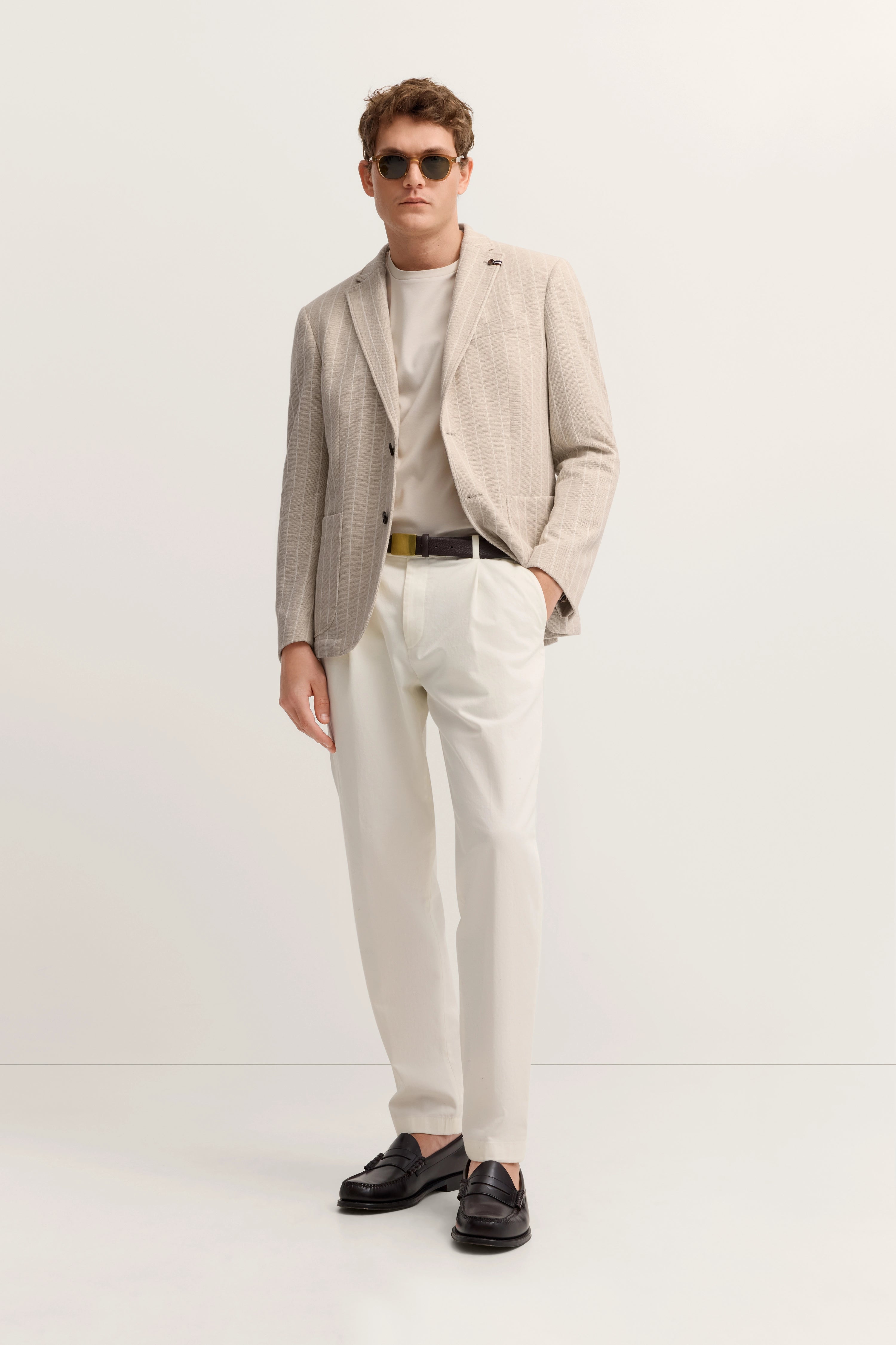 Beiger bugatti Blazer, weißes Shirt und Hose, braune Schuhe. Model stehend, locker elegant.