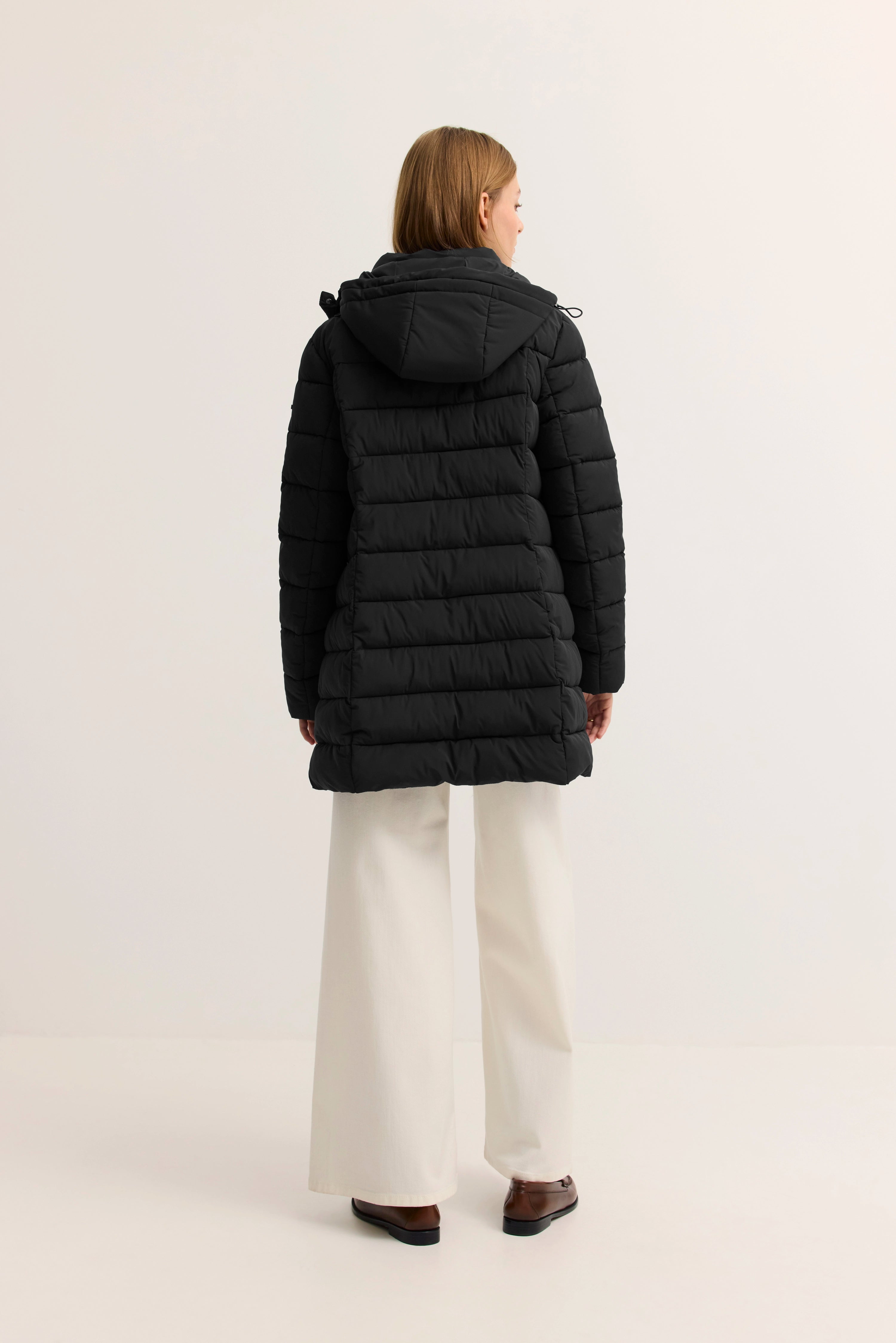 Model in schwarzer bugatti Steppjacke, Rückansicht, mit Kapuze, beige Hose, lässige Pose.