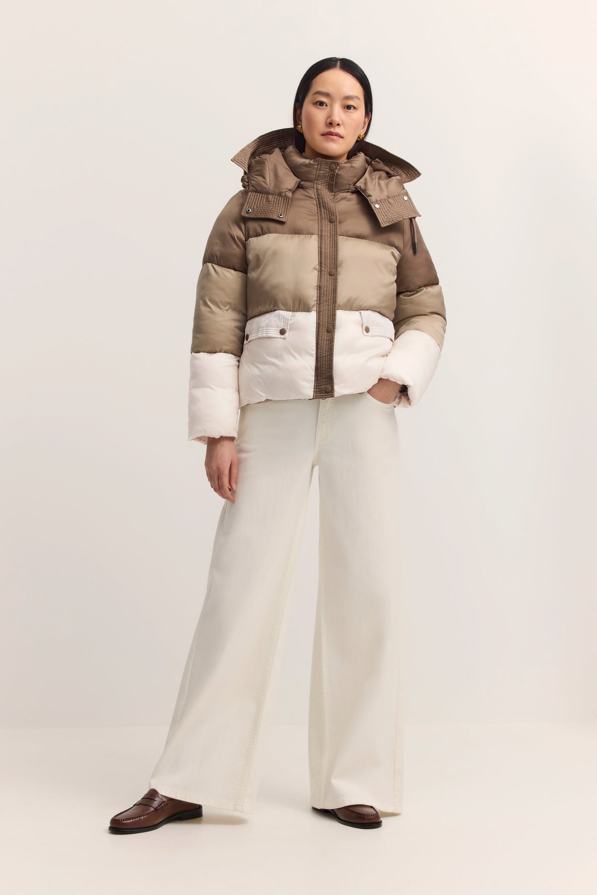 Model in beige-weißer bugatti-Daunenjacke, weißer Hose, braunen Schuhen, stehend.