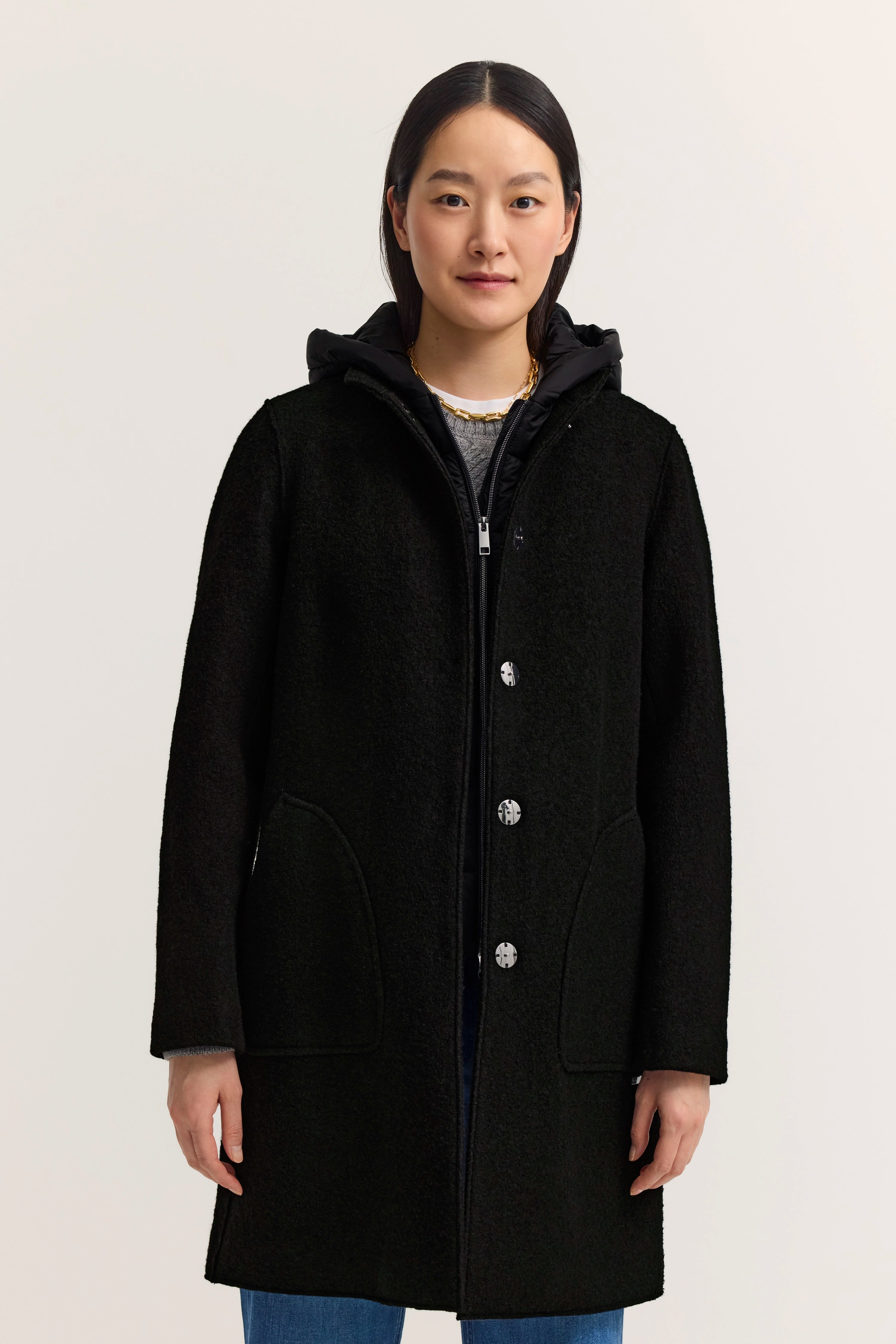 Schwarzer bugatti Mantel auf Model, legeres Stehen, kombiniert mit Jeans und Kapuzenpullover.