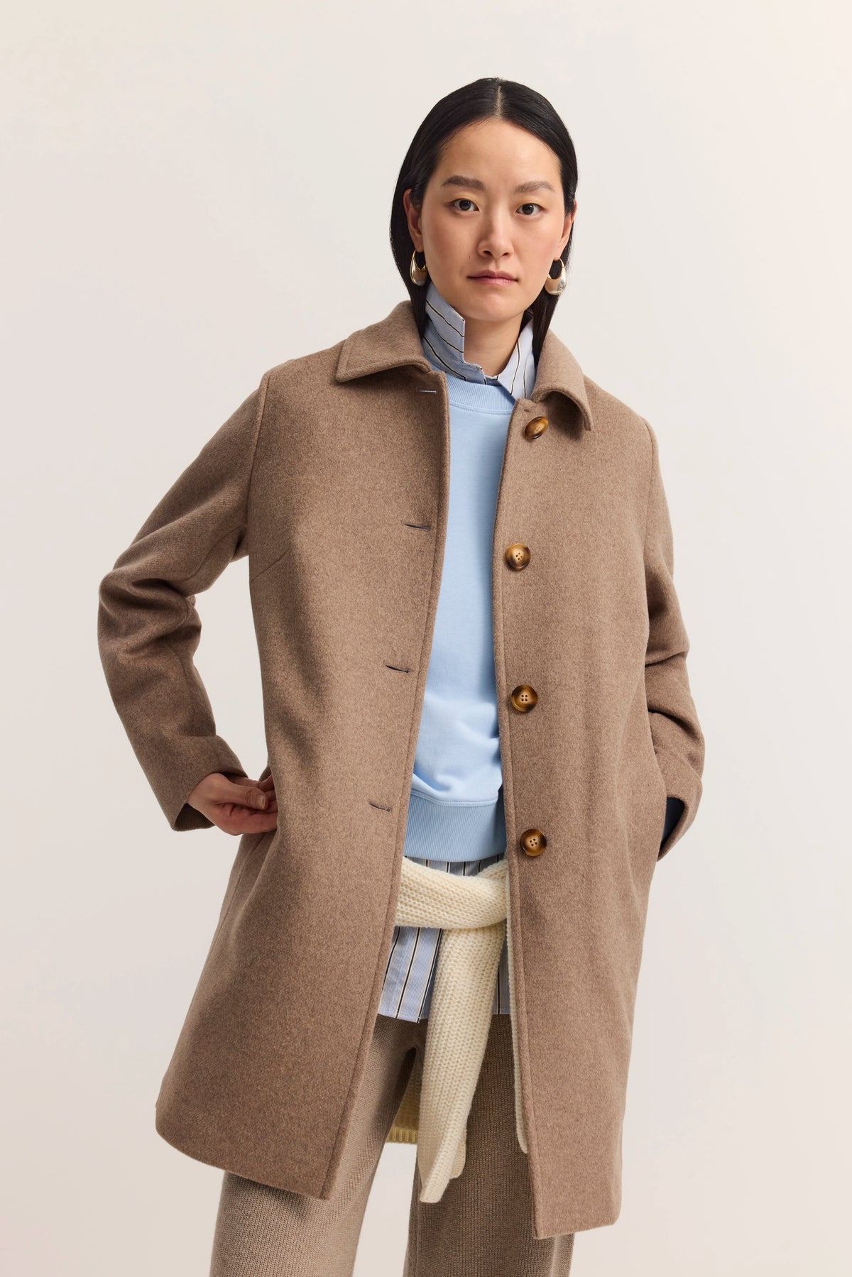 Model in camelbraunem Mantel von bugatti, hellblauer Pullover, gestreiftes Hemd, legeres Posing.