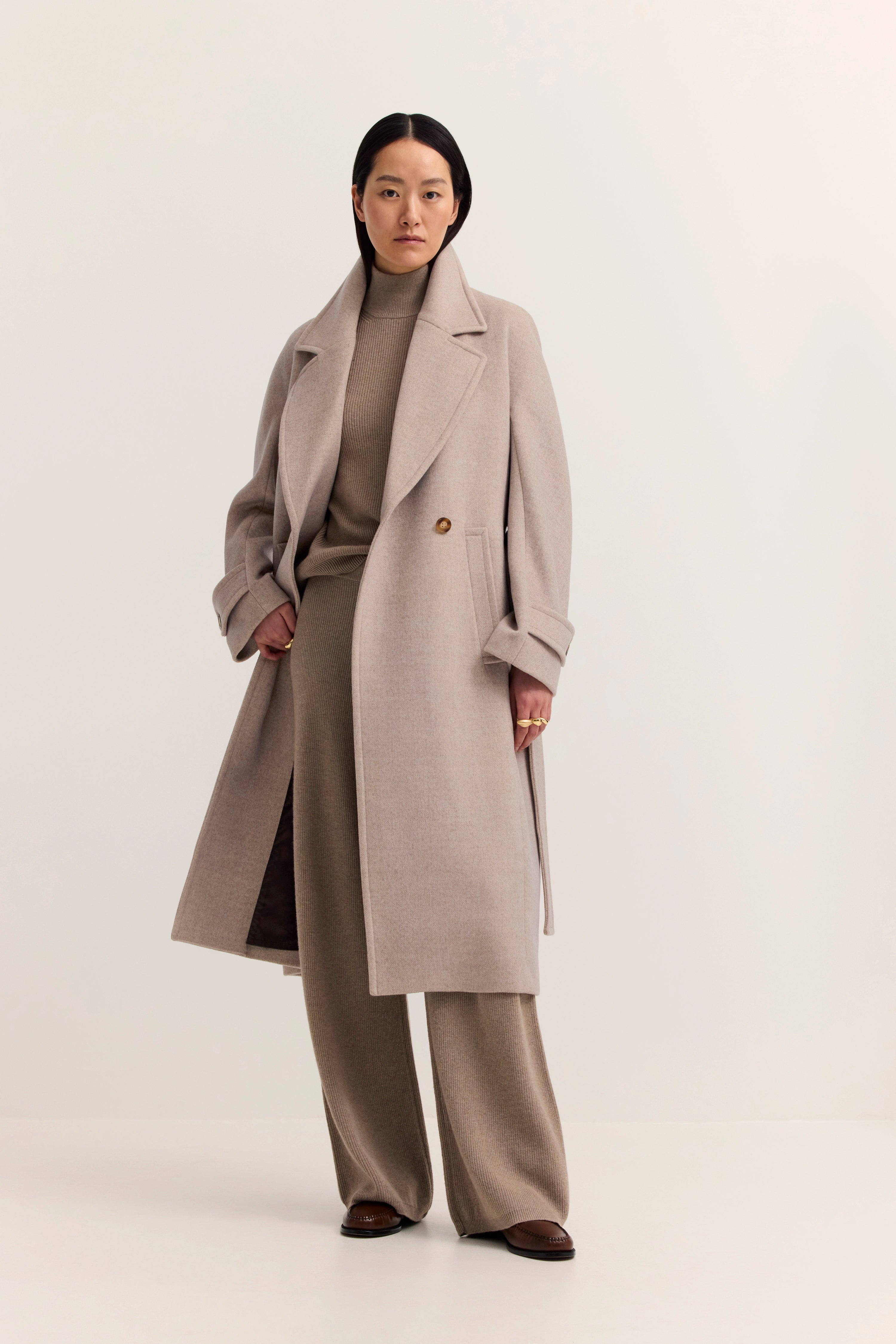 Model in beige bugatti Mantel und Rollkragenpullover, gerade Pose, elegante Ausstrahlung.