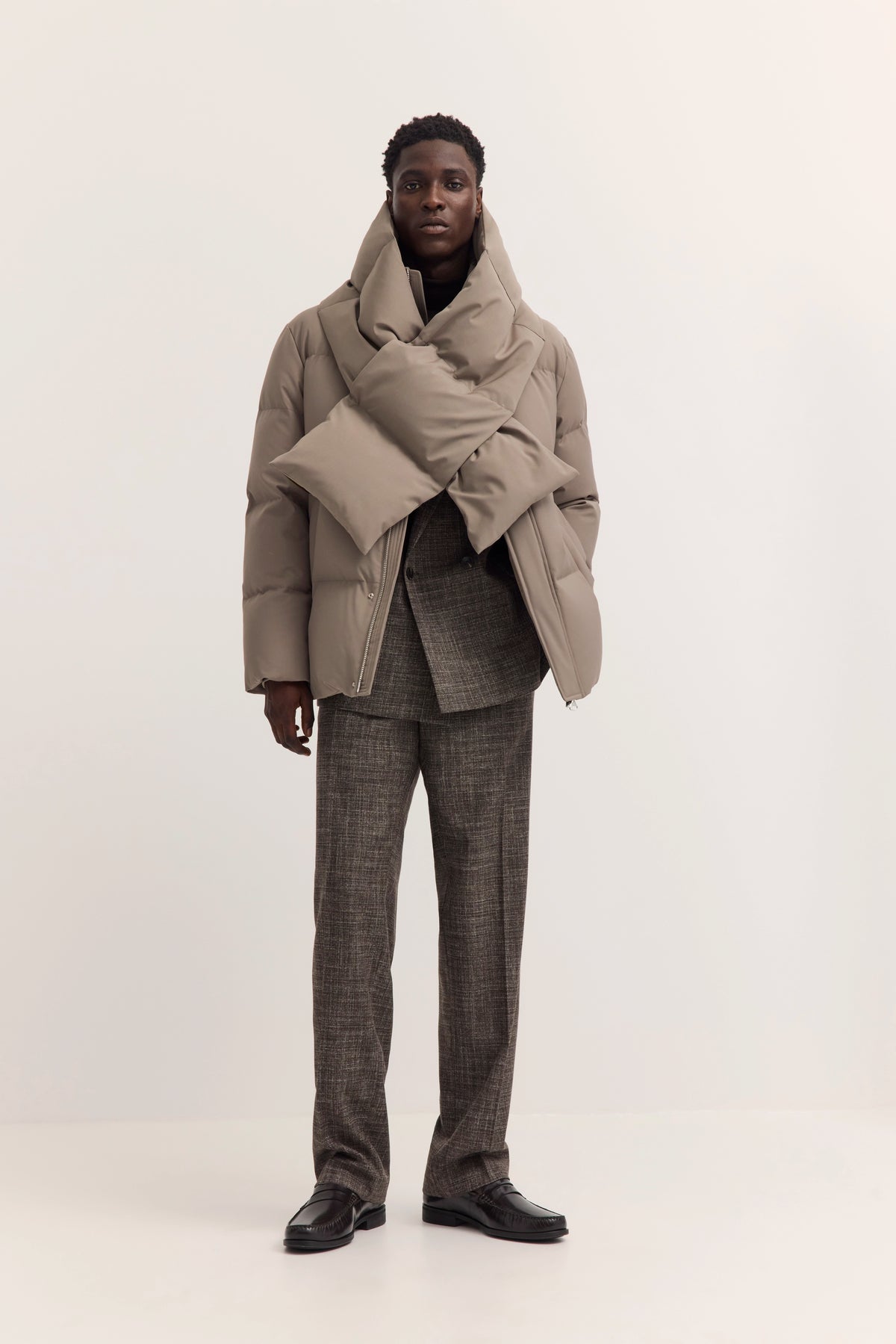 Model in beigefarbener Steppjacke und grauem Anzug von bugatti, frontal stehend.
