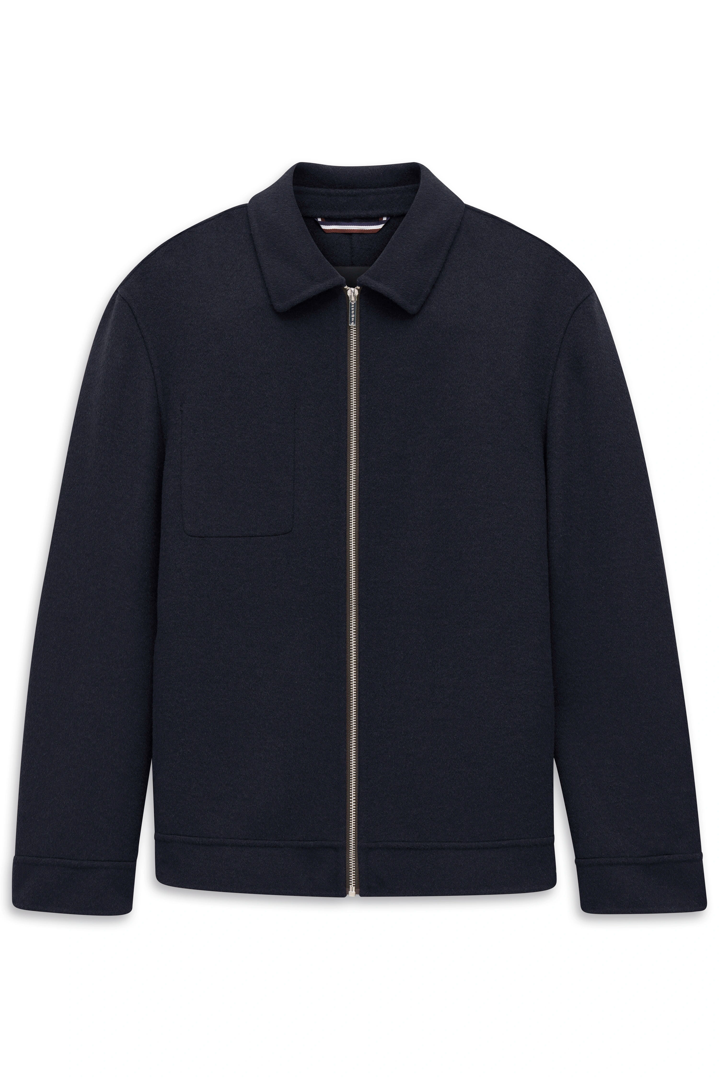 Model in navy Jacke, dunkelblauem Hemd, beige Chino und schwarzen Schuhen, lässiger Stand.