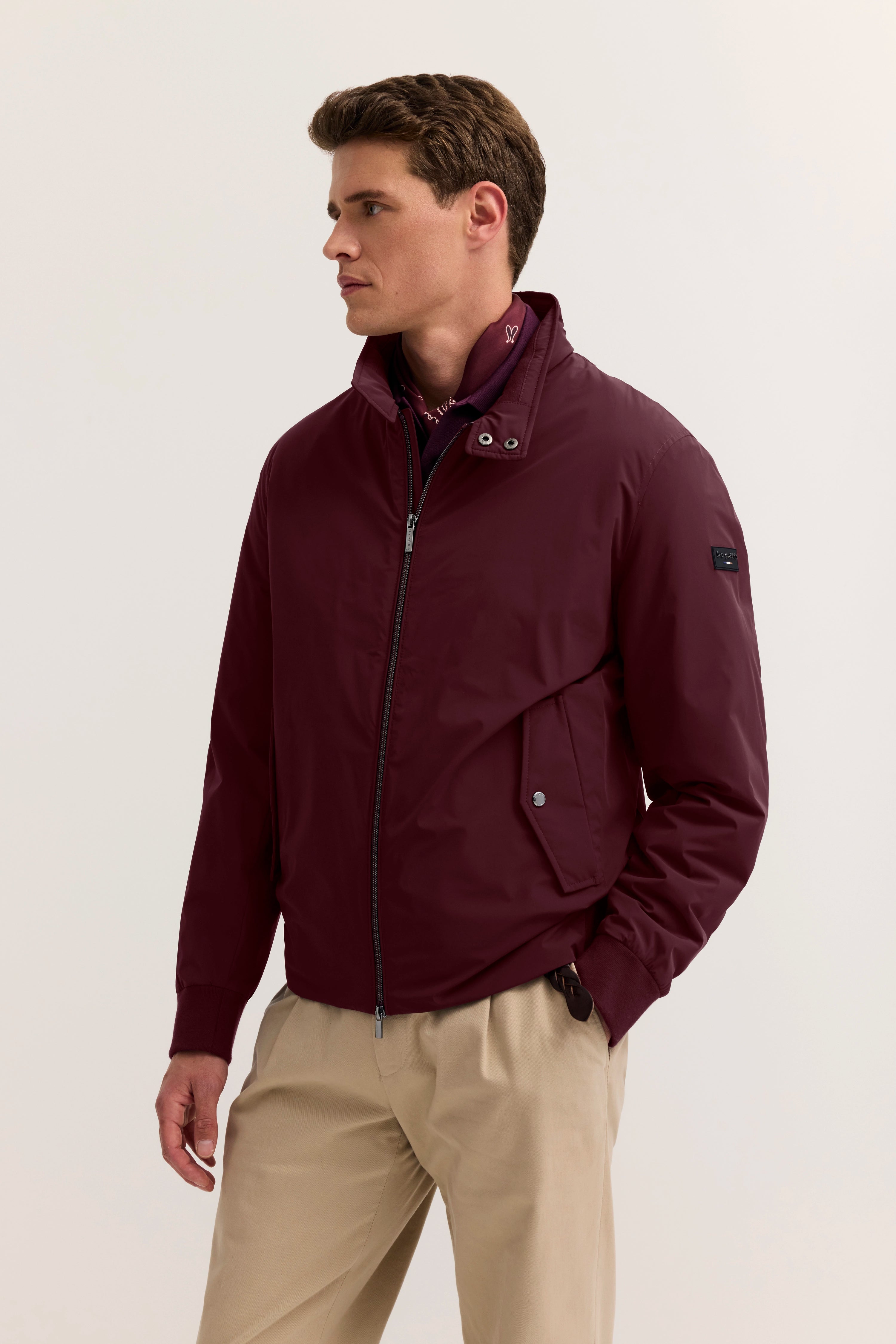 Model im bordeauxfarbenen bugatti-Jacke, seitlich stehend, kombiniert mit beigen Hosen.
