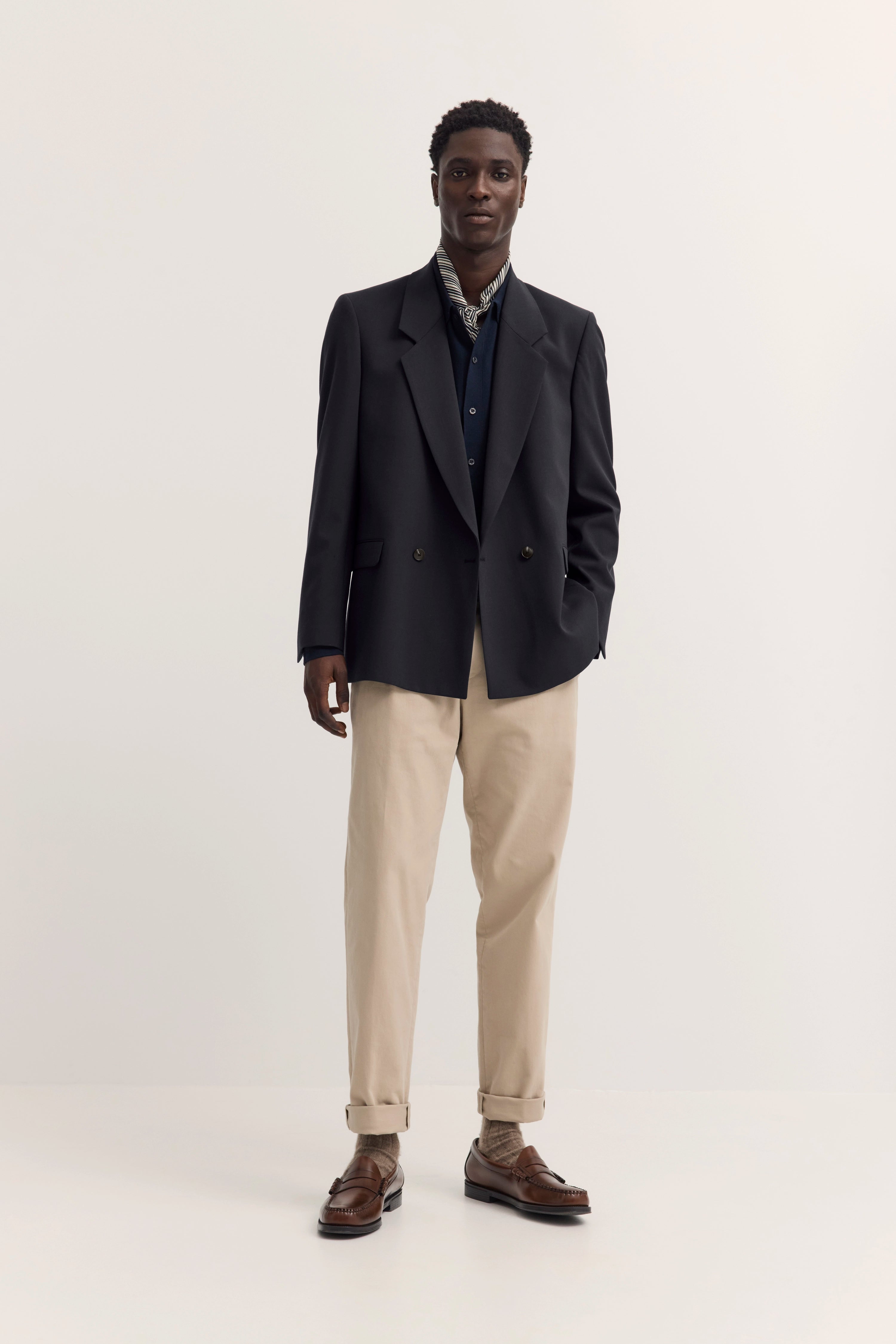 Model in schwarzem Blazer, beiger Hose, braunen Schuhen, legeres Posing.