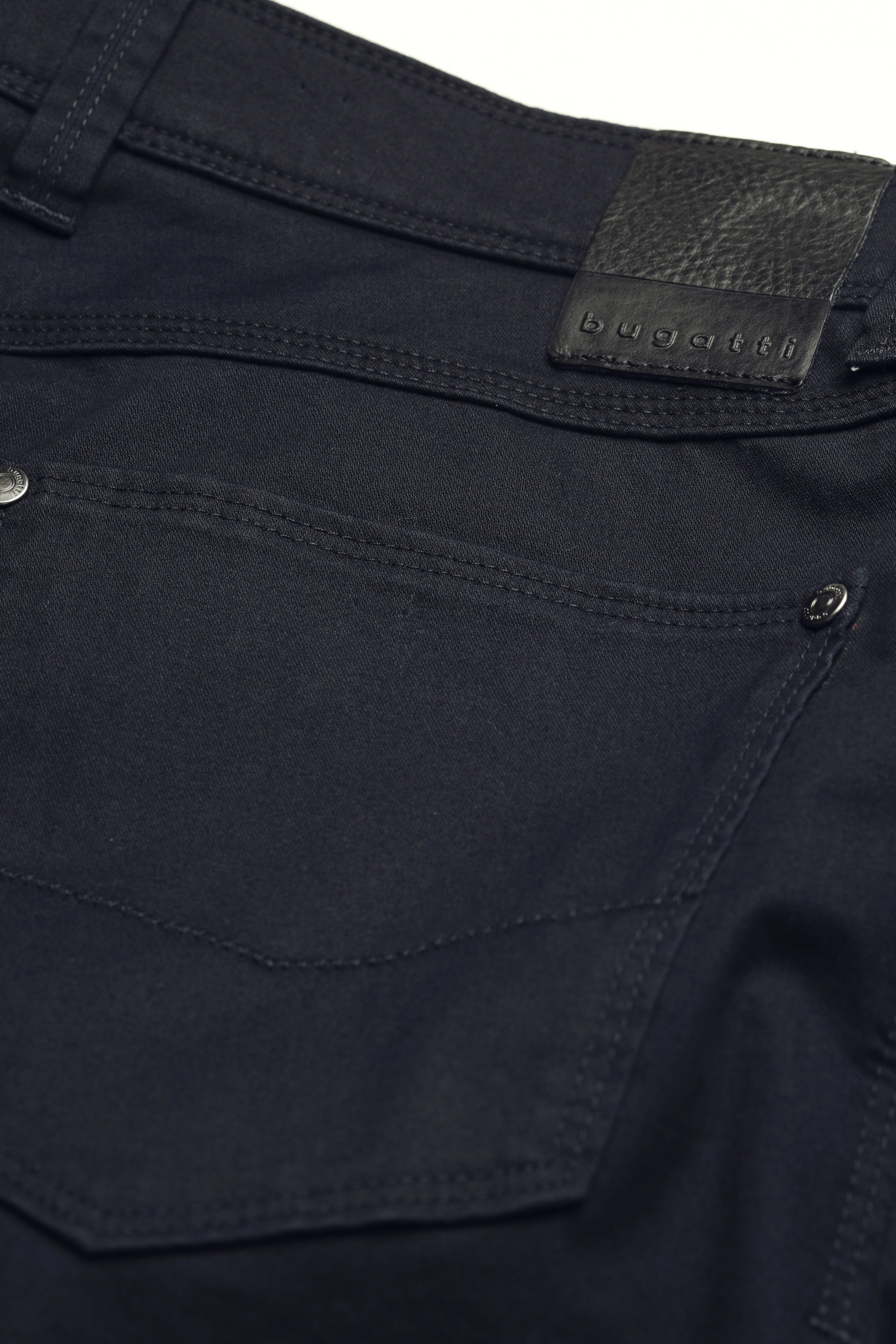 Nahaufnahme einer dunkelblauen bugatti-Jeans mit silbernen Knöpfen und Label.