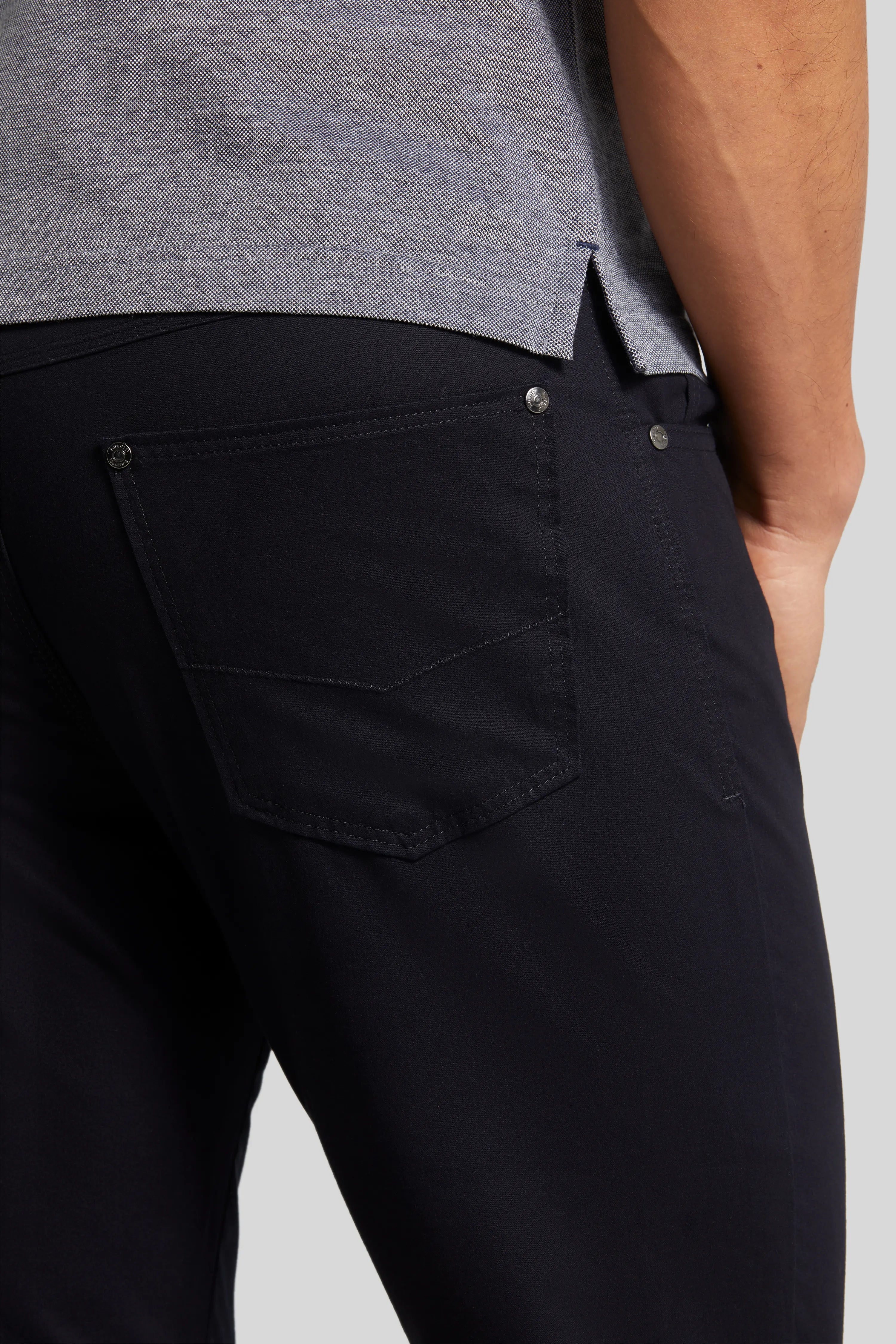 Schwarze bugatti Hose, leger getragen mit grauem Shirt und weißen Sneakern, Model zeigt Rückansicht.