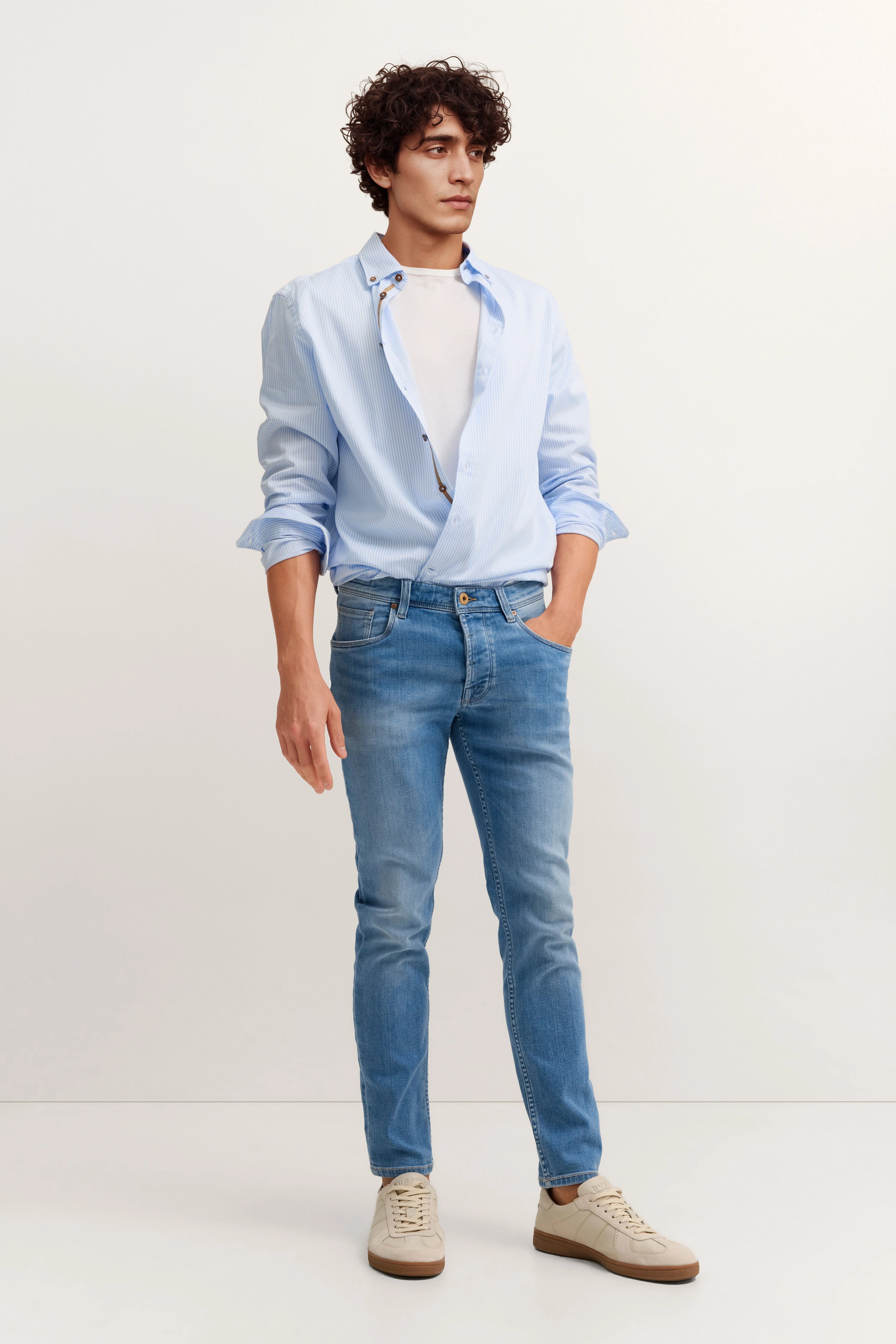 Model in hellblauem Hemd, weißem T-Shirt, blauen Jeans, beigen Sneakern