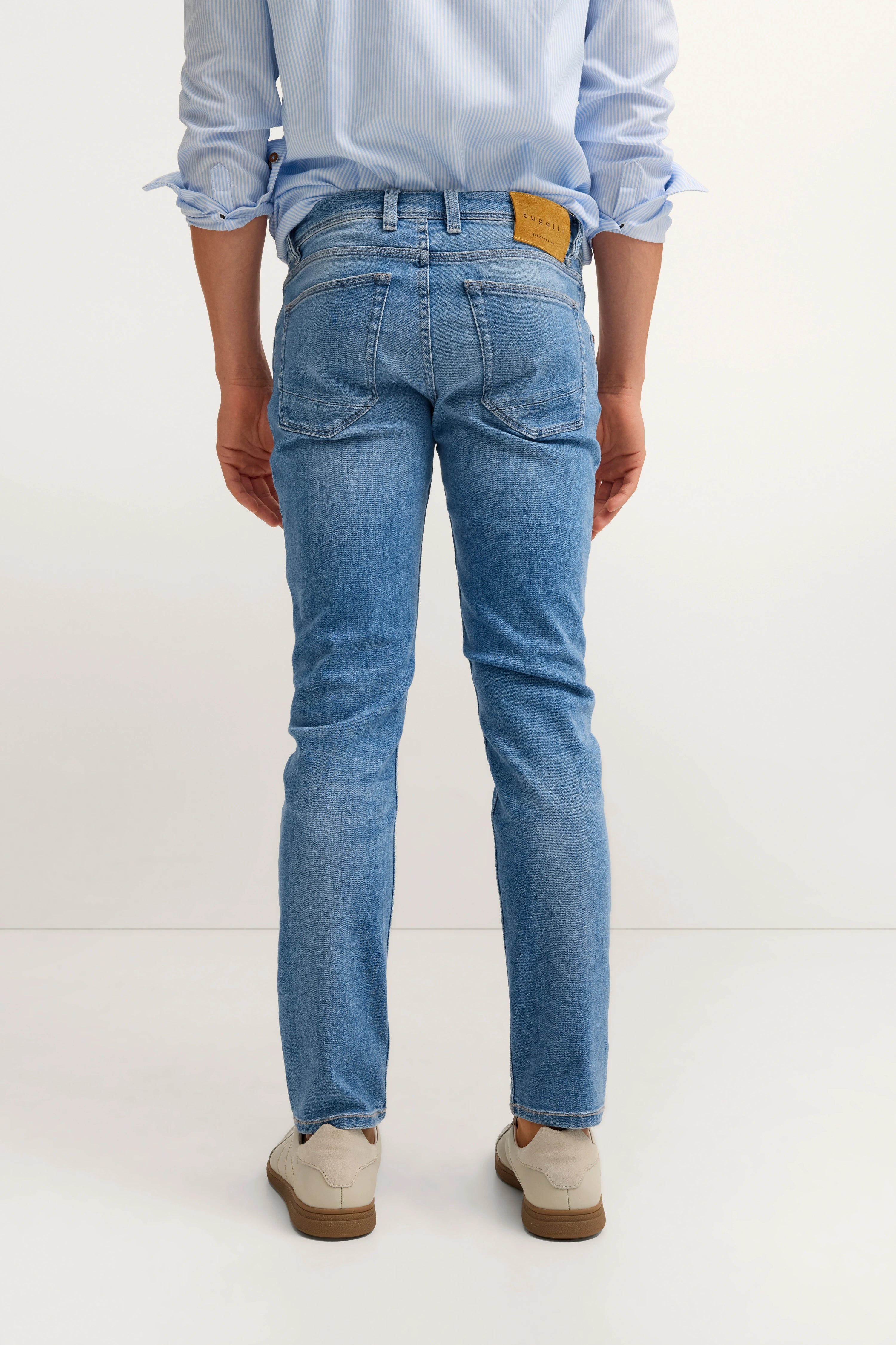 Herrenmodell in blauer Jeans und hellblauem Hemd von bugatti, Rückansicht, legeres Posing.