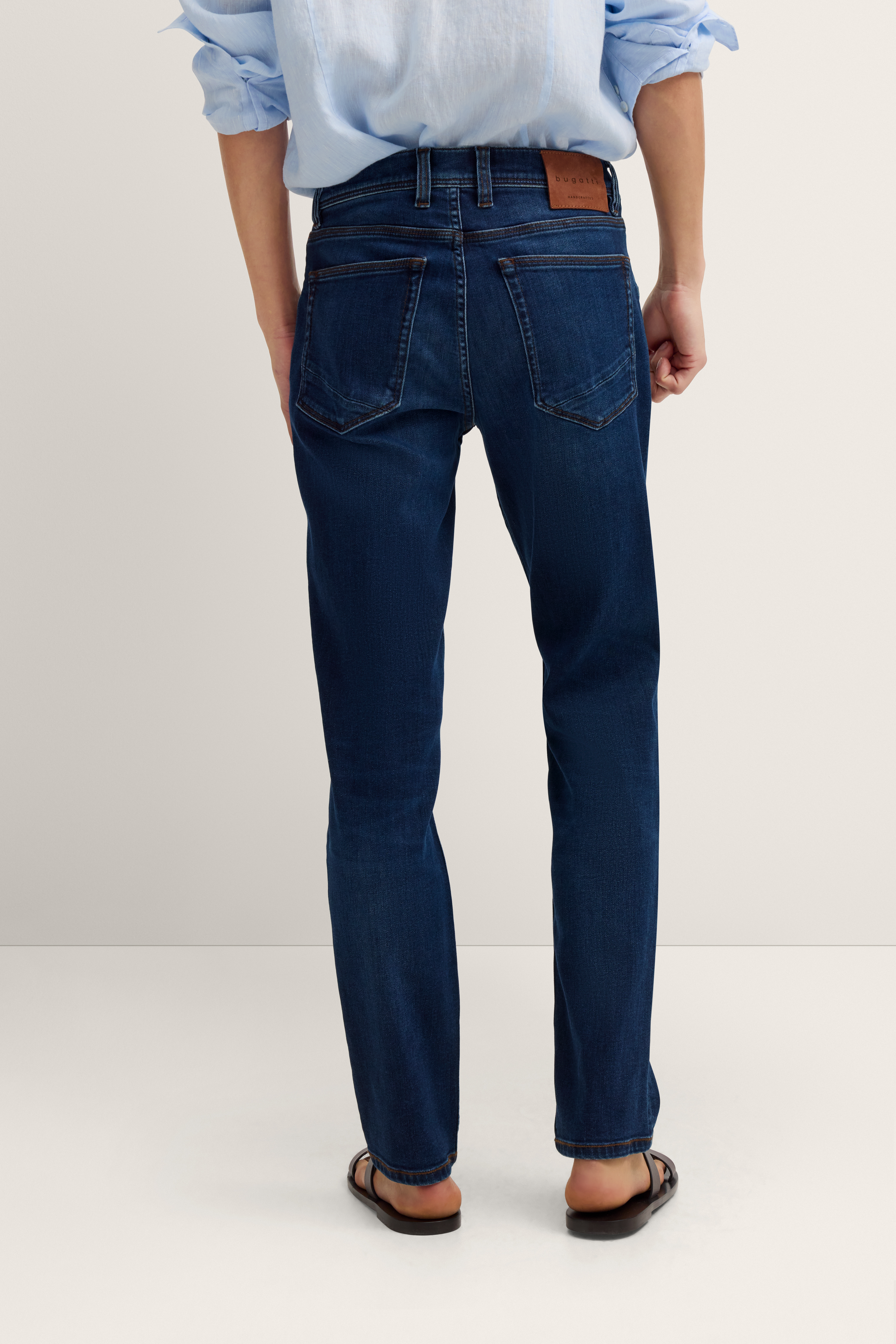 Dunkelblaue Jeans von bugatti, legeres Modelbild, Rückansicht, lässiges Stehen in Sandalen.