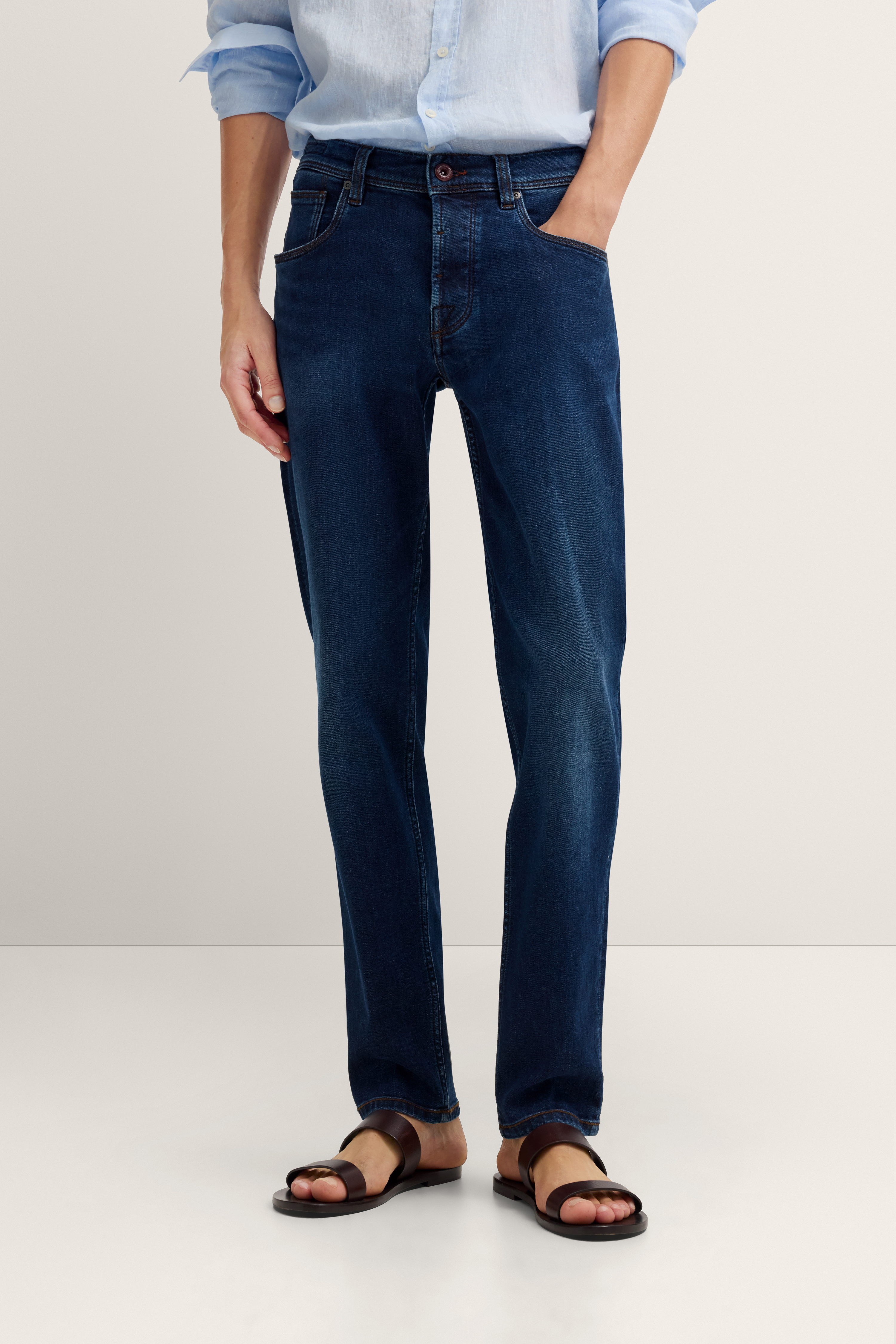 Dunkelblaue Jeans mit hellblauem Hemd, legeres Modelbild, Hände in Hosentaschen.