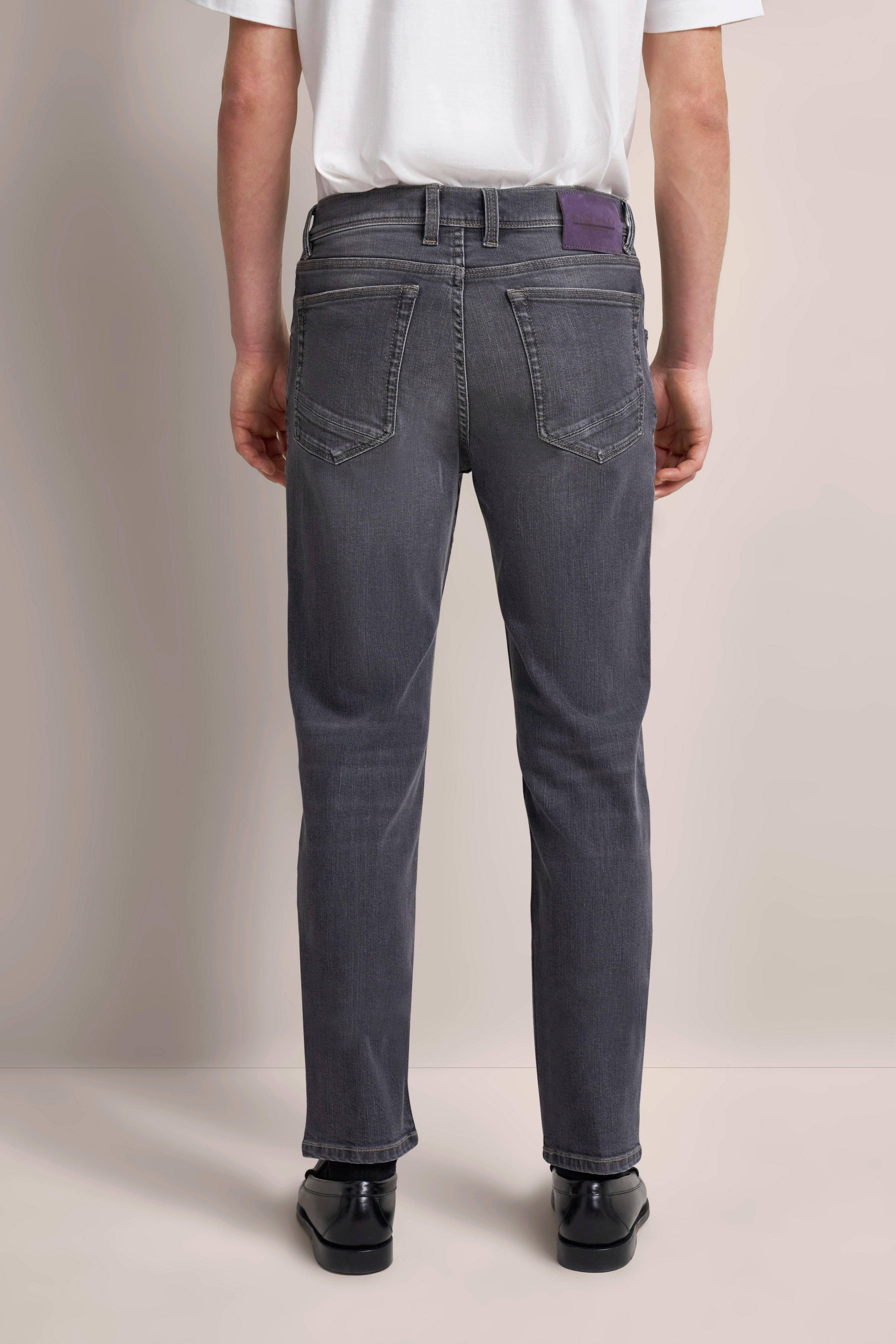 Graue Jeans, Rückansicht, Modellbild, entspannte Pose, kombiniert mit schwarzem Schuh, weißes Oberteil.