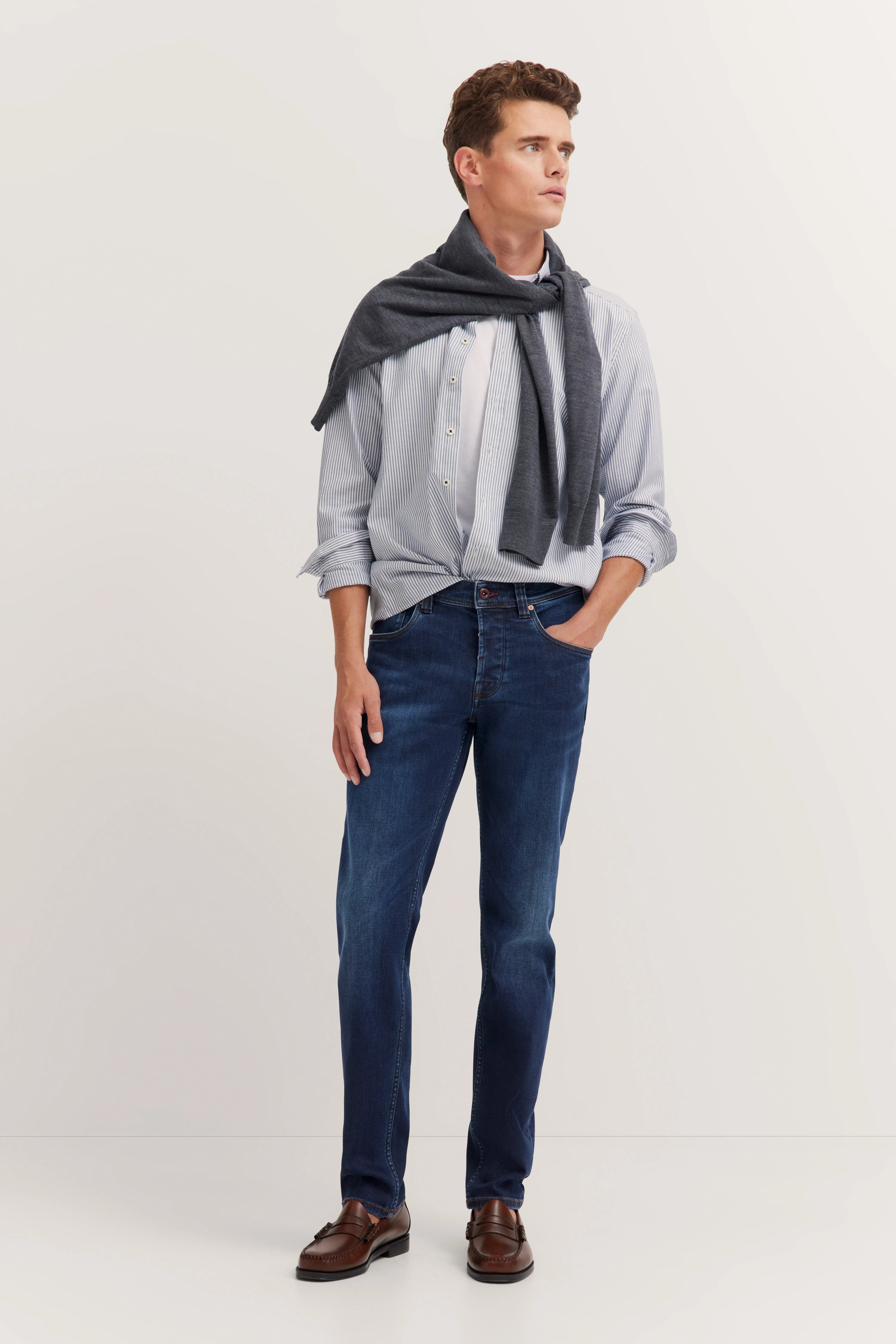 Model trägt blaue Jeans mit gestreiftem Hemd, Rückansicht. bugatti-Label sichtbar. Elegant und zeitlos.