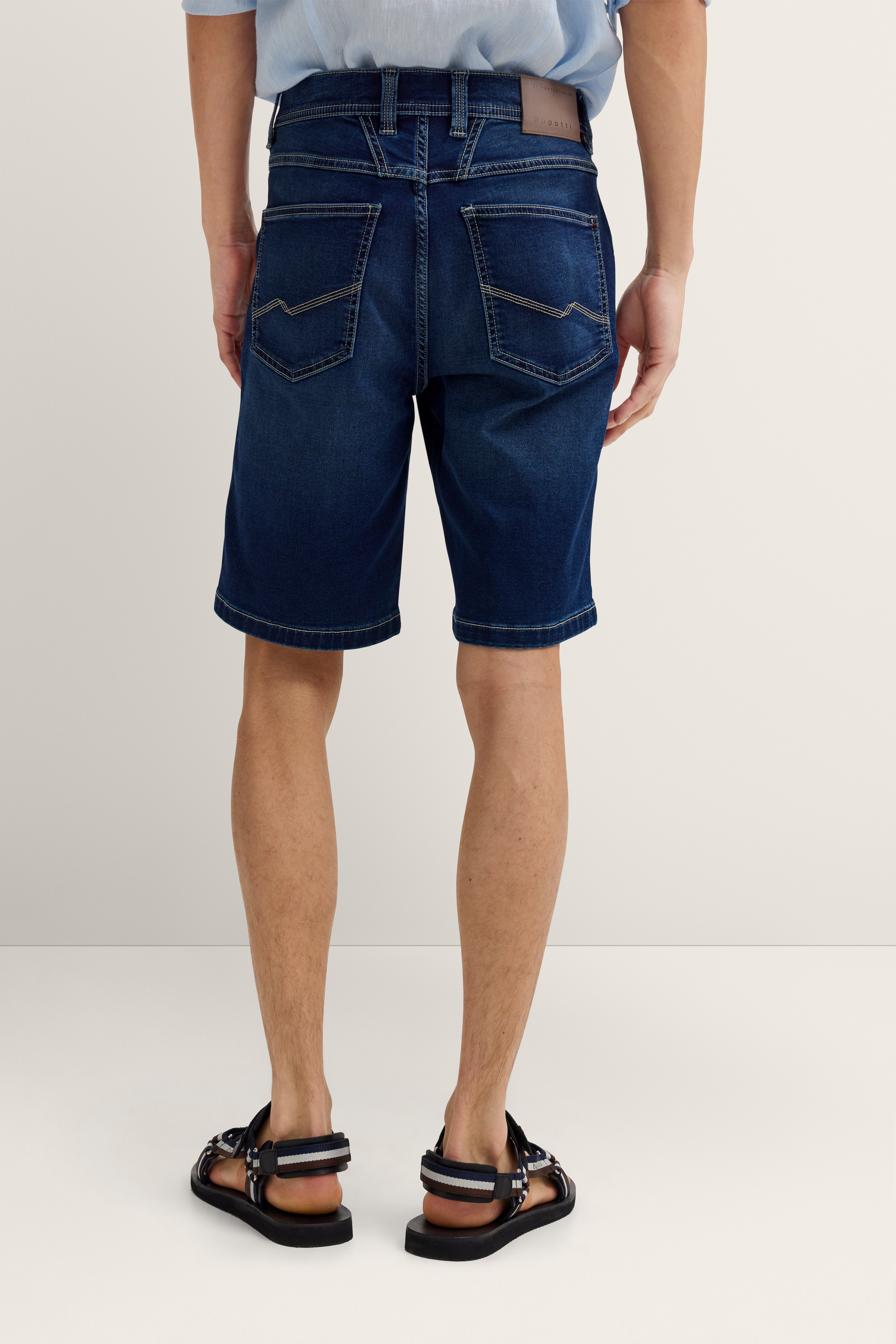 bugatti Jeansshorts, dunkelblau, Model von hinten, lässiger Stand, Sandalen.