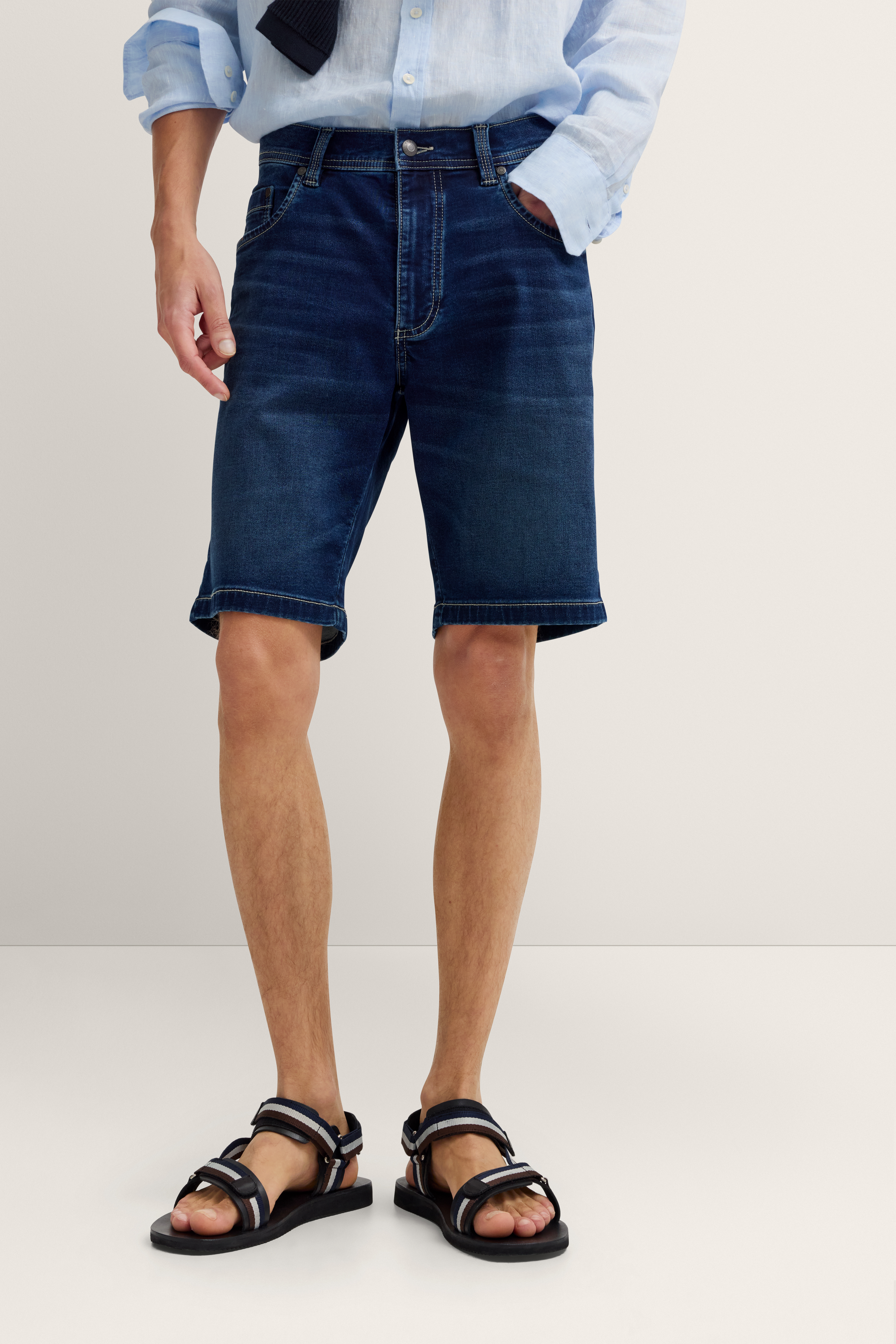 Bugatti Outfit: Blaues Hemd, dunkelblaue Jeansshorts, schwarze Sandalen. Legerbild ohne Gesicht.