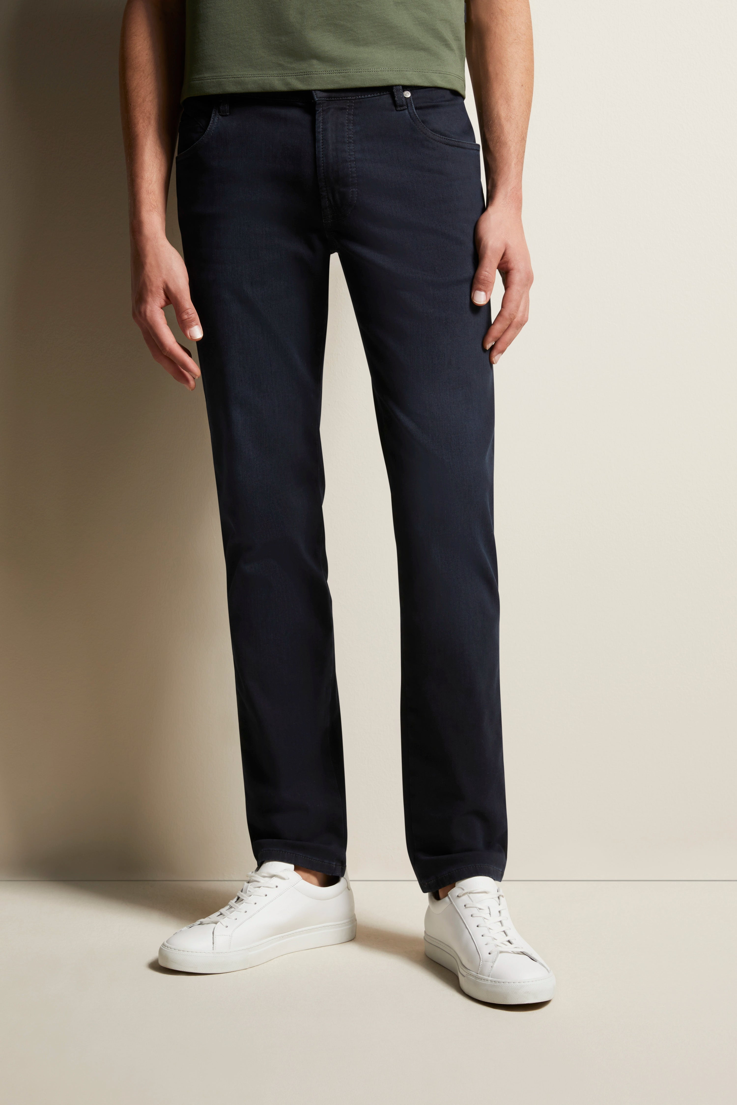 Green T-shirt, dark blue jeans, white sneakers. Model standing, relaxed look, embodying bugatti's refined Italian style.