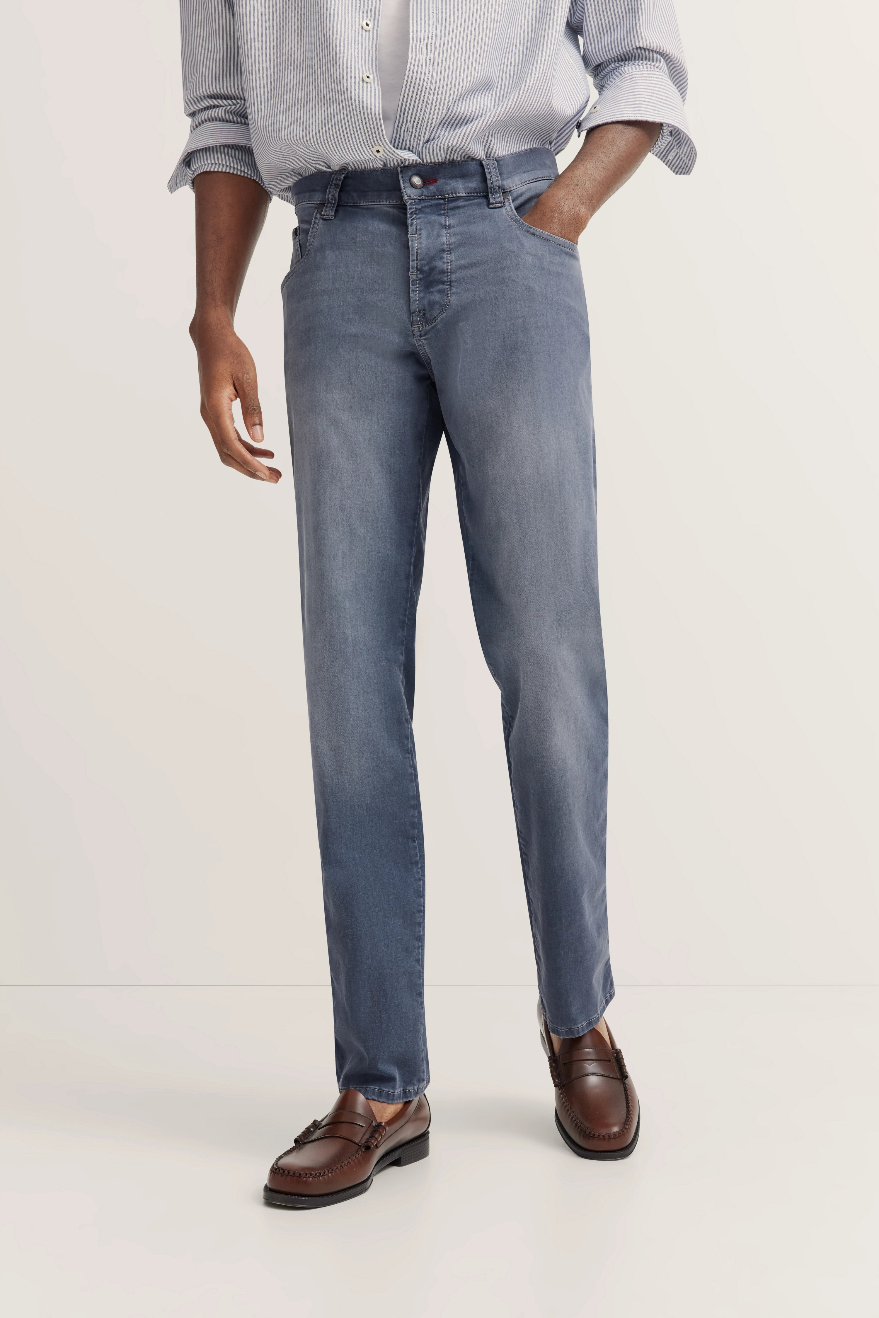 Legeres Modelbild von bugatti: blaue Jeans, gestreiftes Hemd, braune Loafer, entspannte Pose.