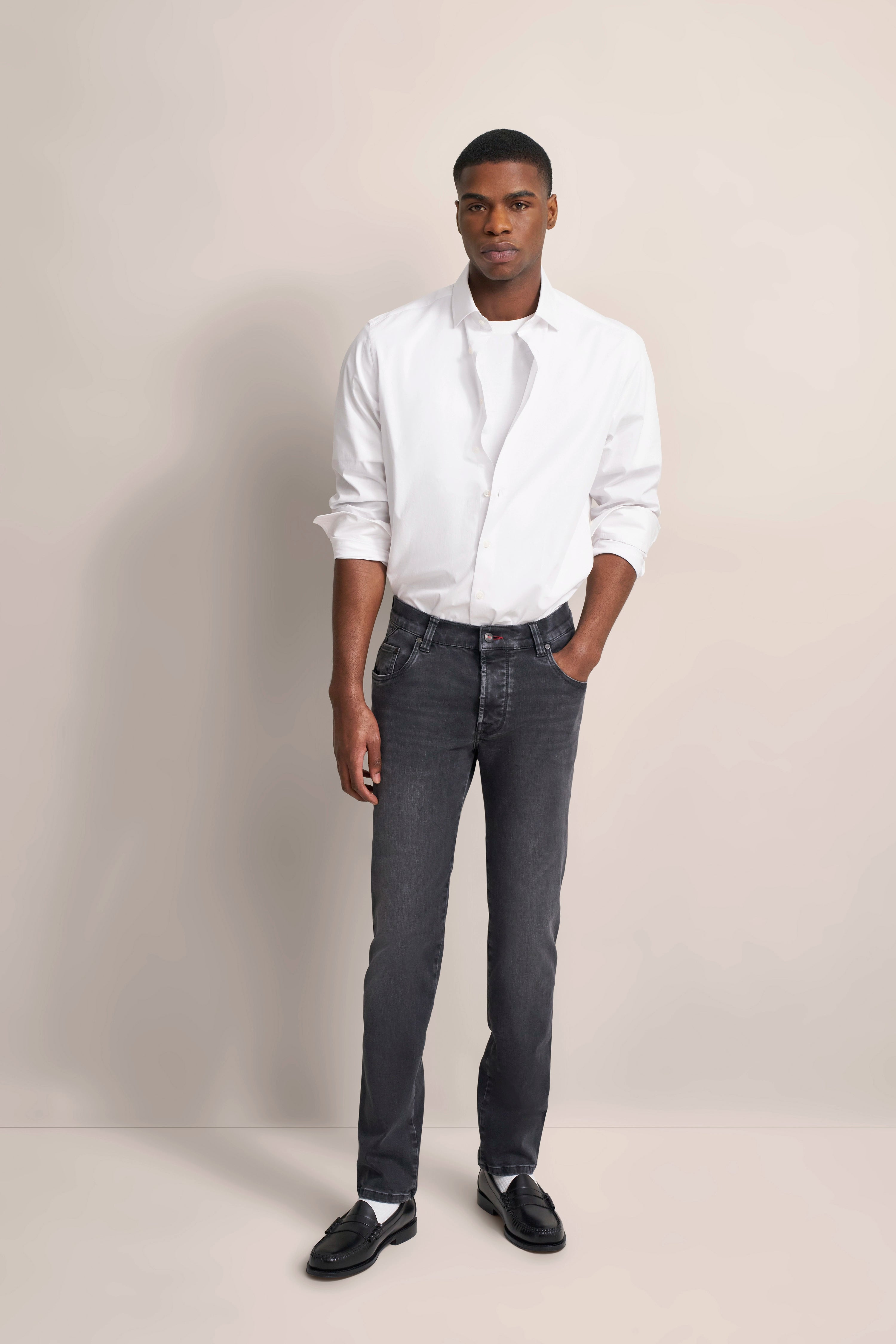 Elegant model: White shirt, grey jeans, black shoes. Relaxed pose, one hand in pocket.