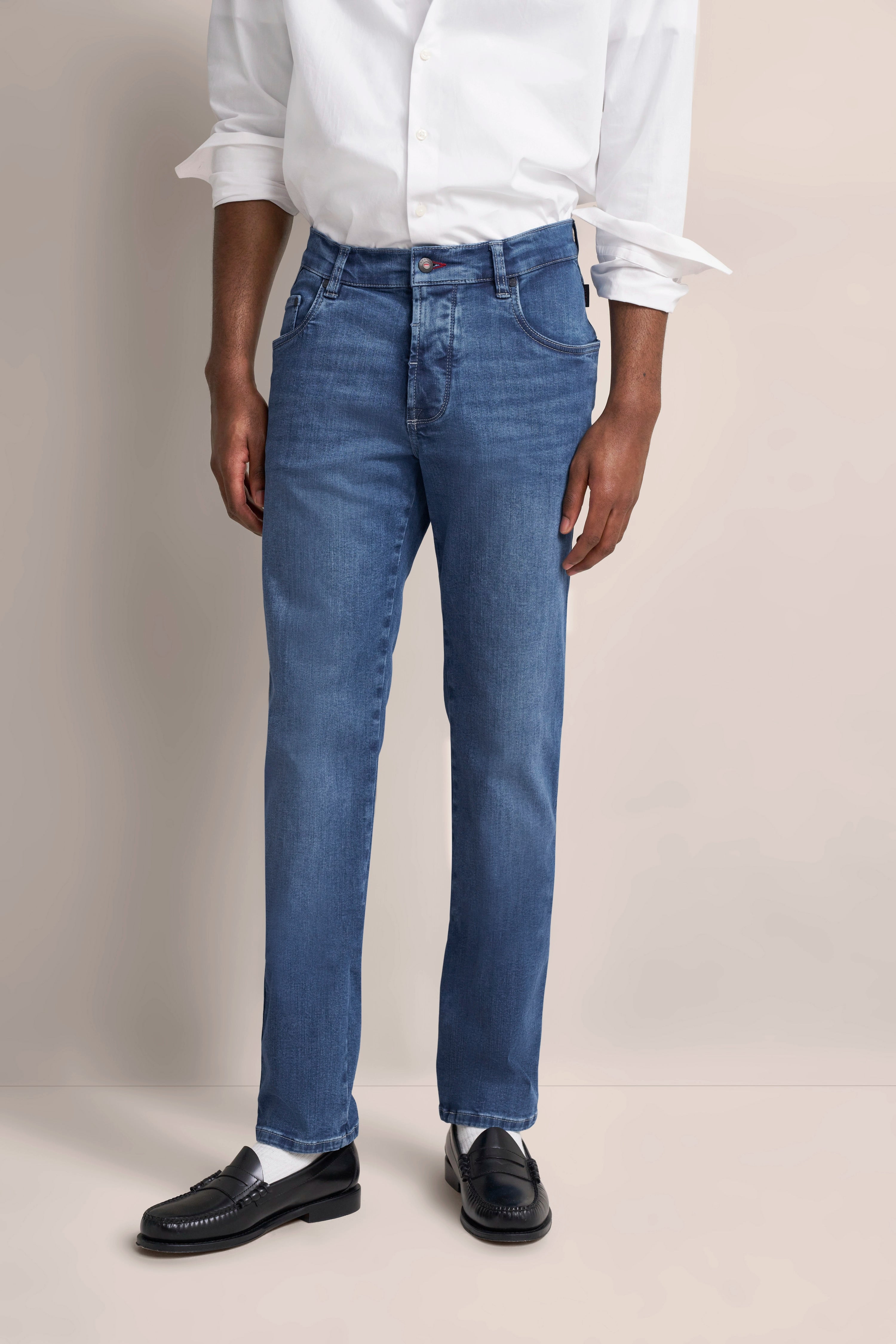 Weiße Hemd und blaue Jeans, legeres Modelbild, lockere Pose, schwarze Loafer.