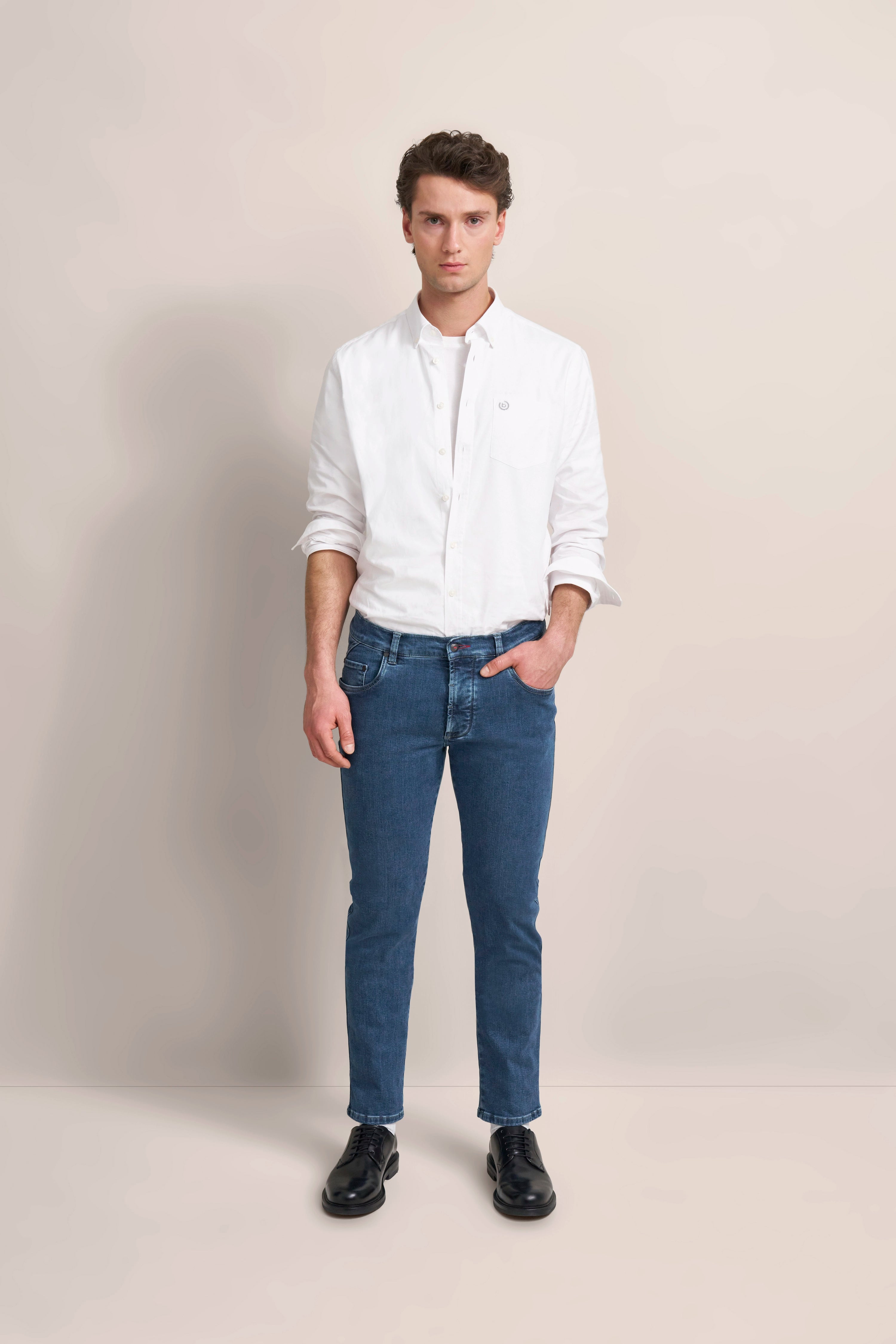Weißes Hemd, blaue Jeans, schwarze Schuhe, Modelbild, lässige Pose.