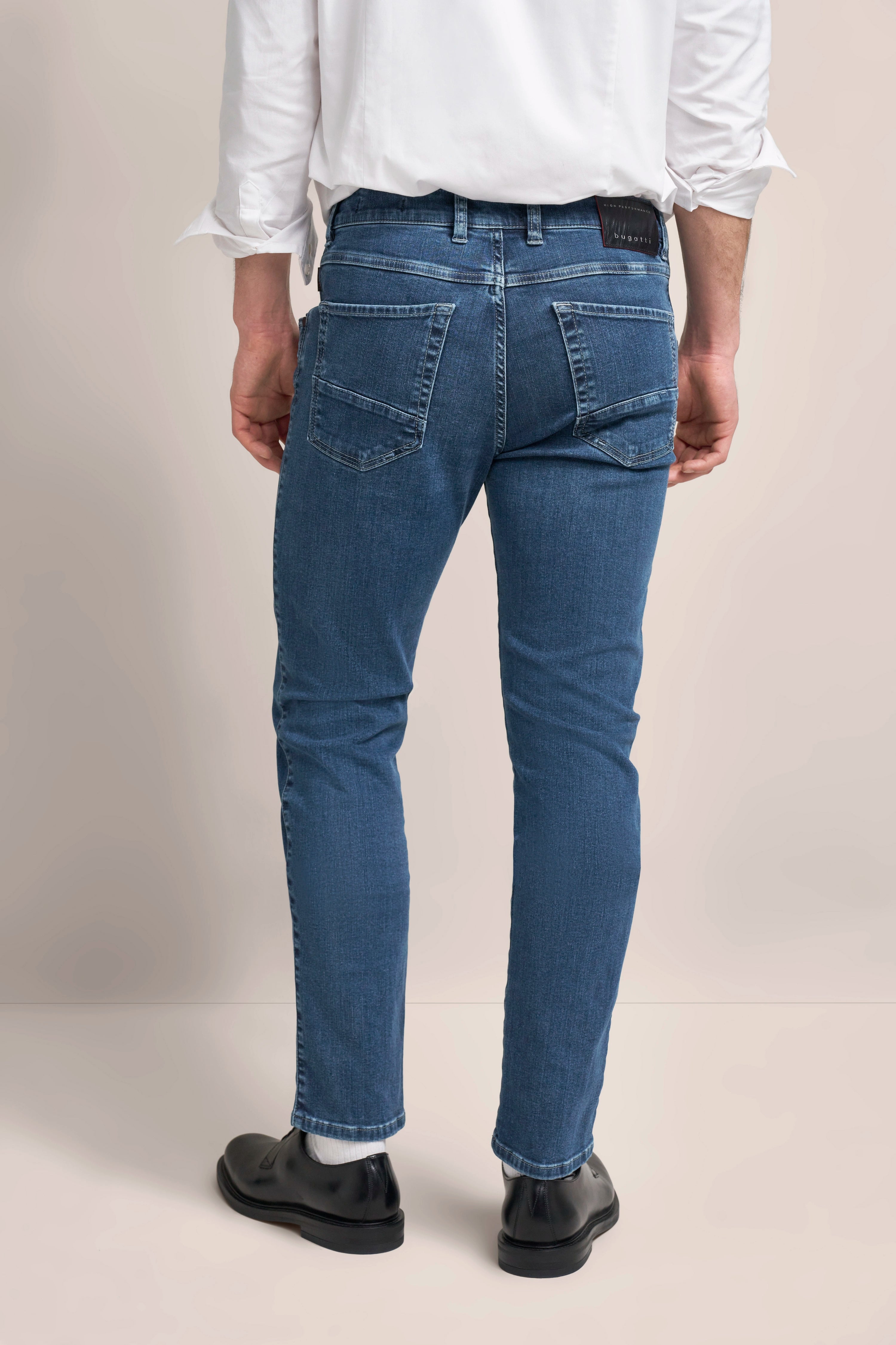 bugatti model: man in blue jeans & white shirt, casually standing, shiny black shoes.