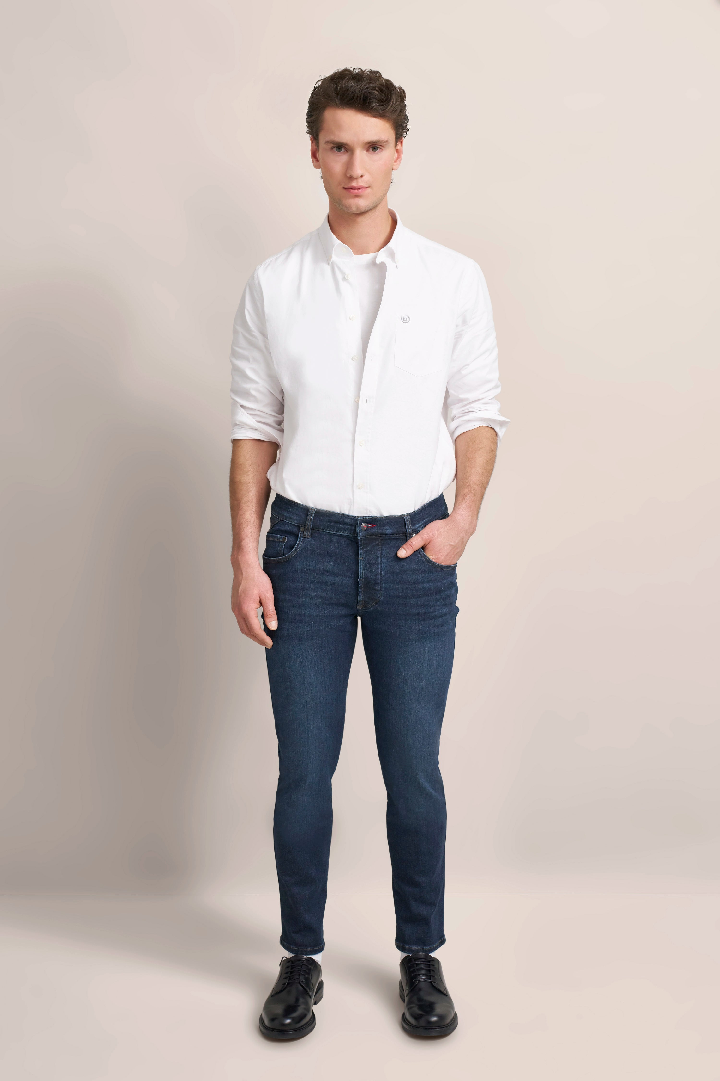 Weißes Hemd, blaue Jeans, schwarze Schuhe. Modelbild, entspanntes Posing. bugatti Stil.