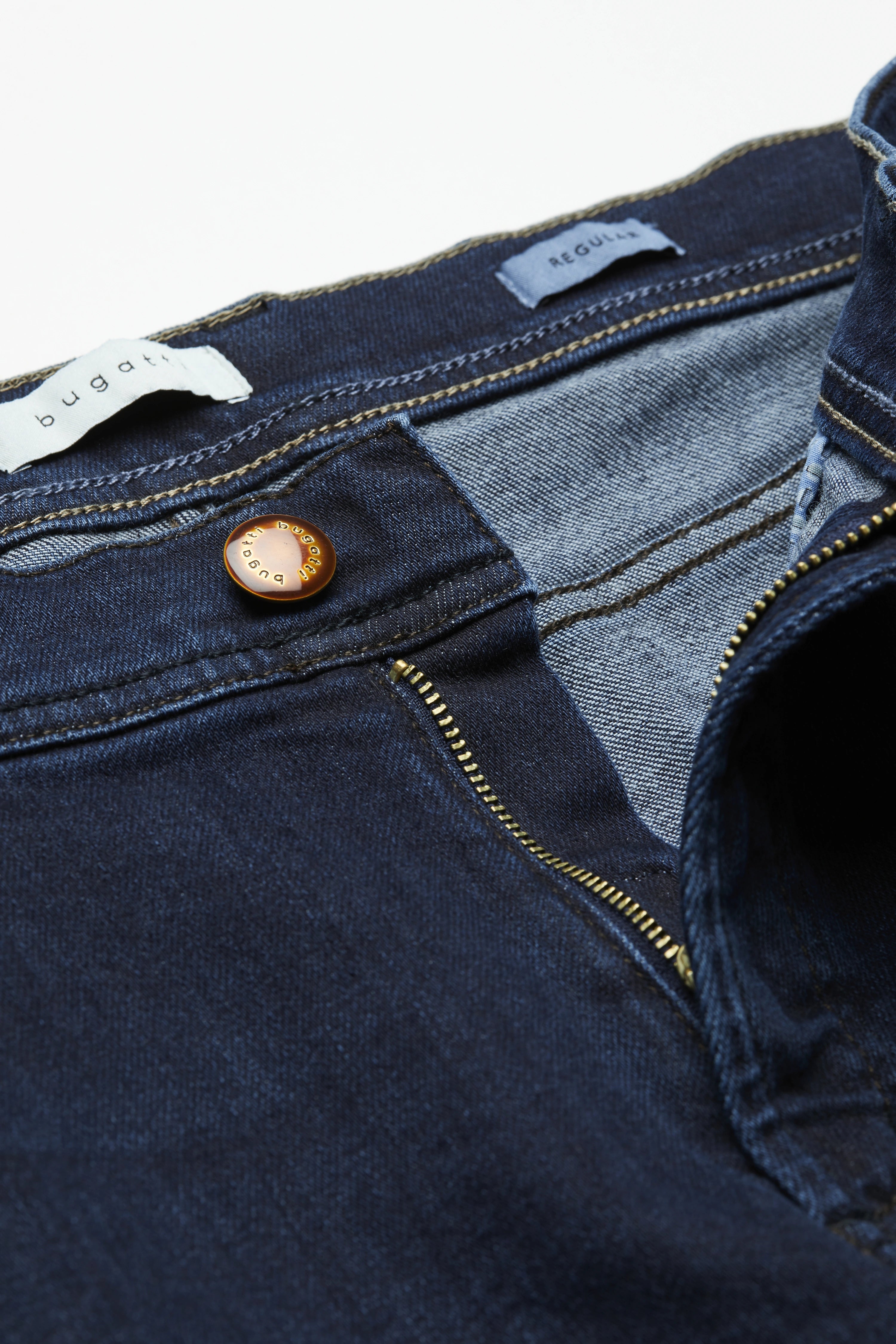 Dunkelblaue bugatti Jeans mit goldener Knopfleiste und Reißverschluss, Detailaufnahme.
