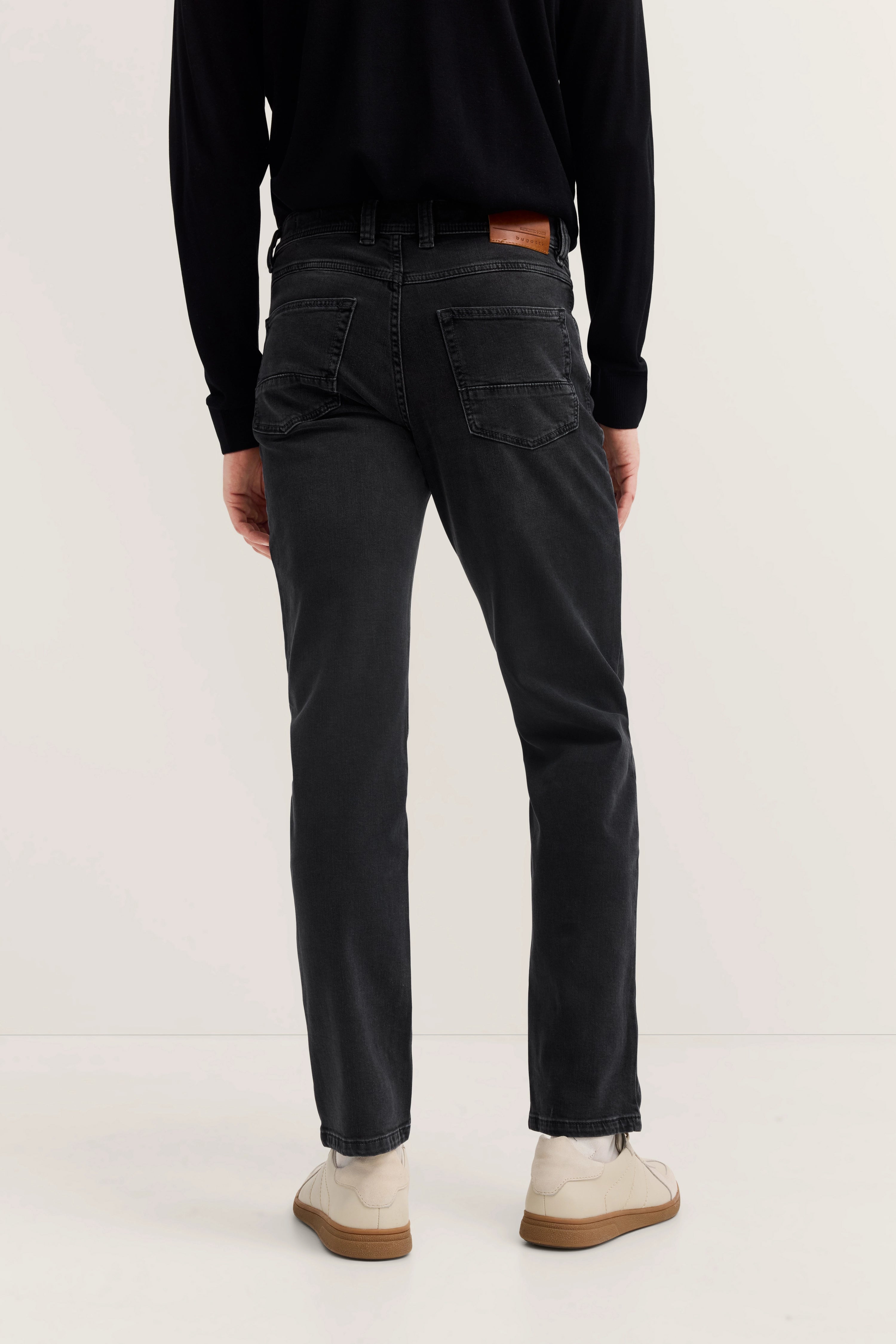 Schwarze Jeans von bugatti, Modelbild von hinten, lässige Pose, weiße Sneakers, eleganter Look.