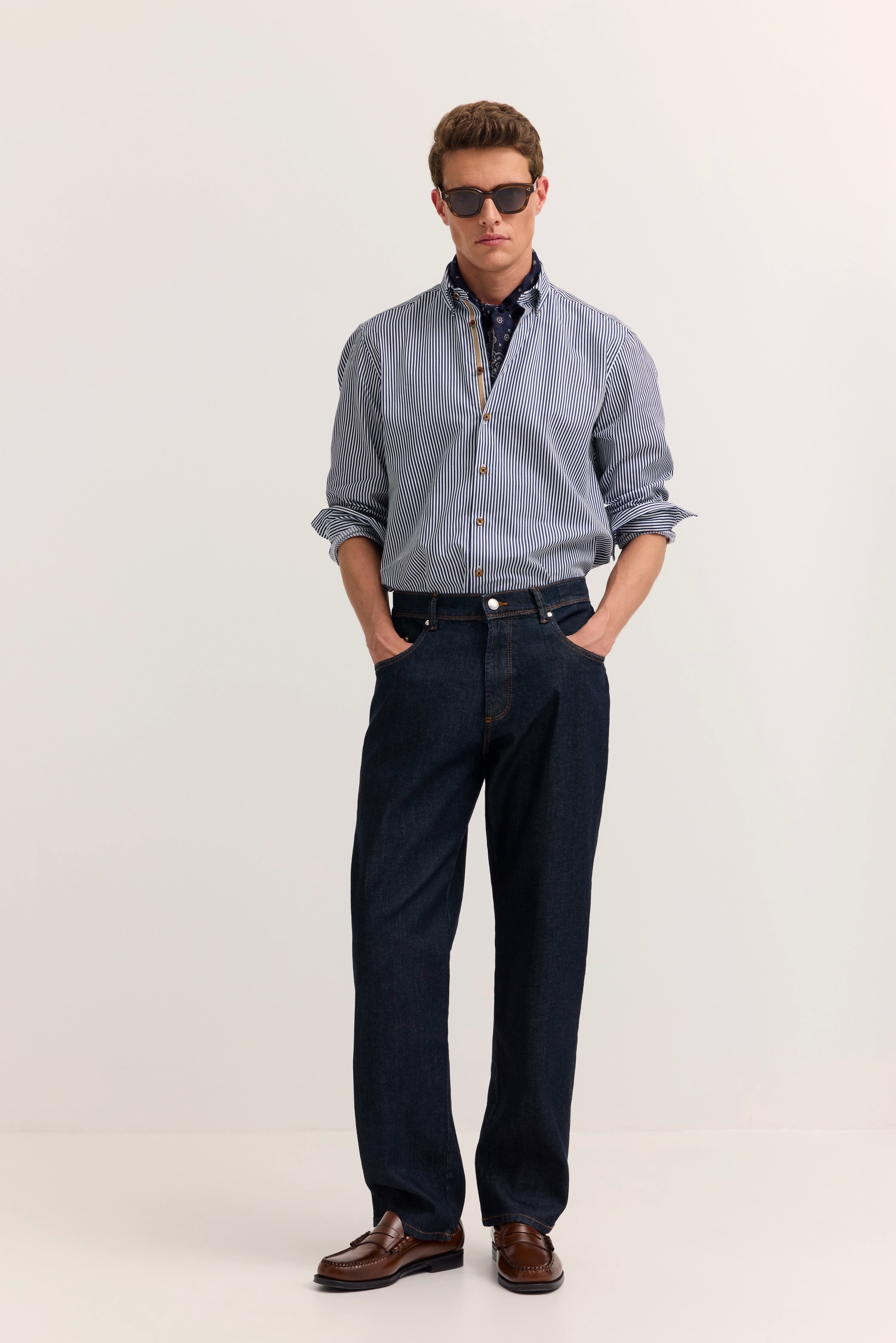bugatti Model in gestreiftem Hemd, dunkelblauer Jeans, braune Schuhe, lässiges Posing.