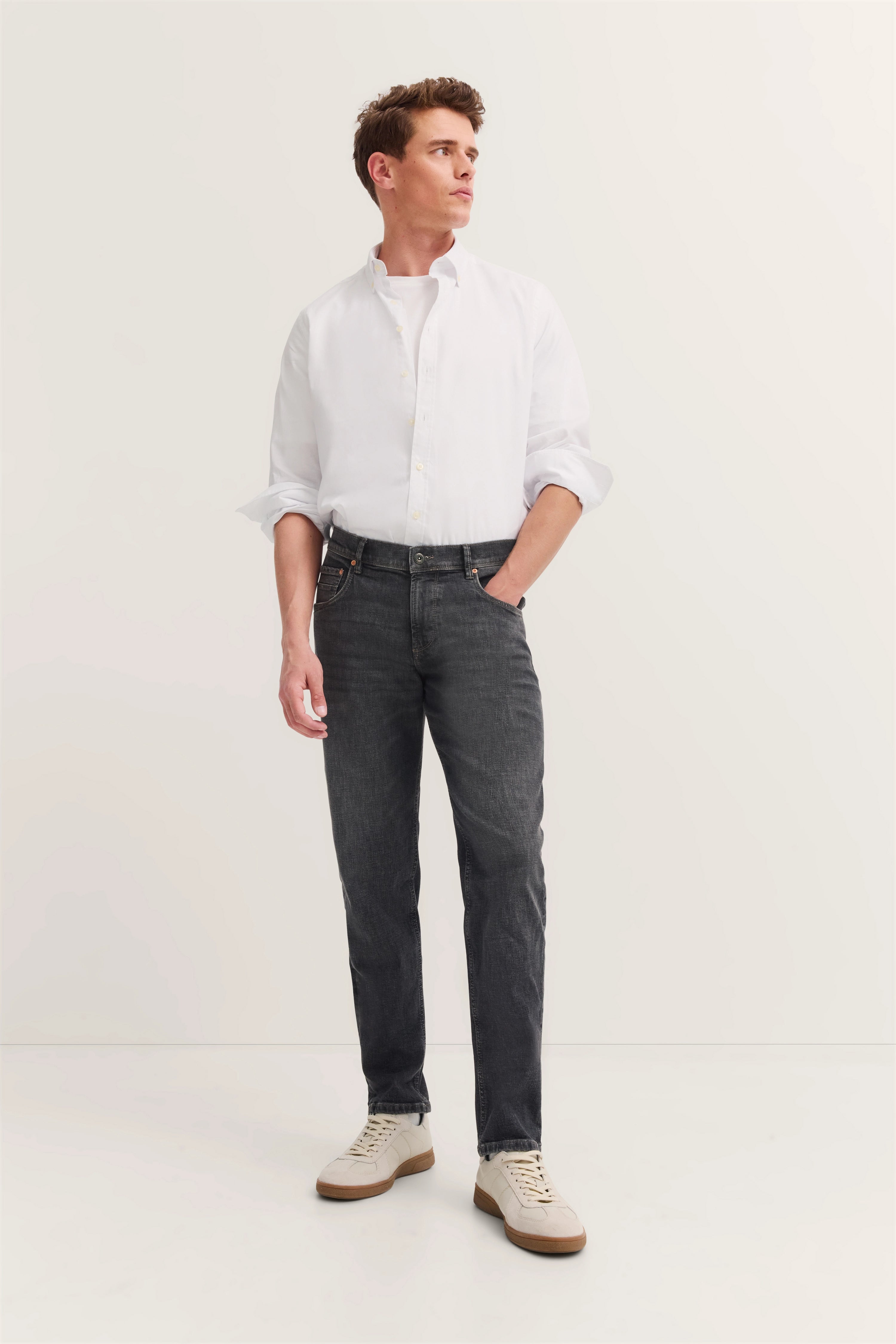 White shirt, gray jeans, cream sneakers, model stands casually, bugatti style and sophistication.