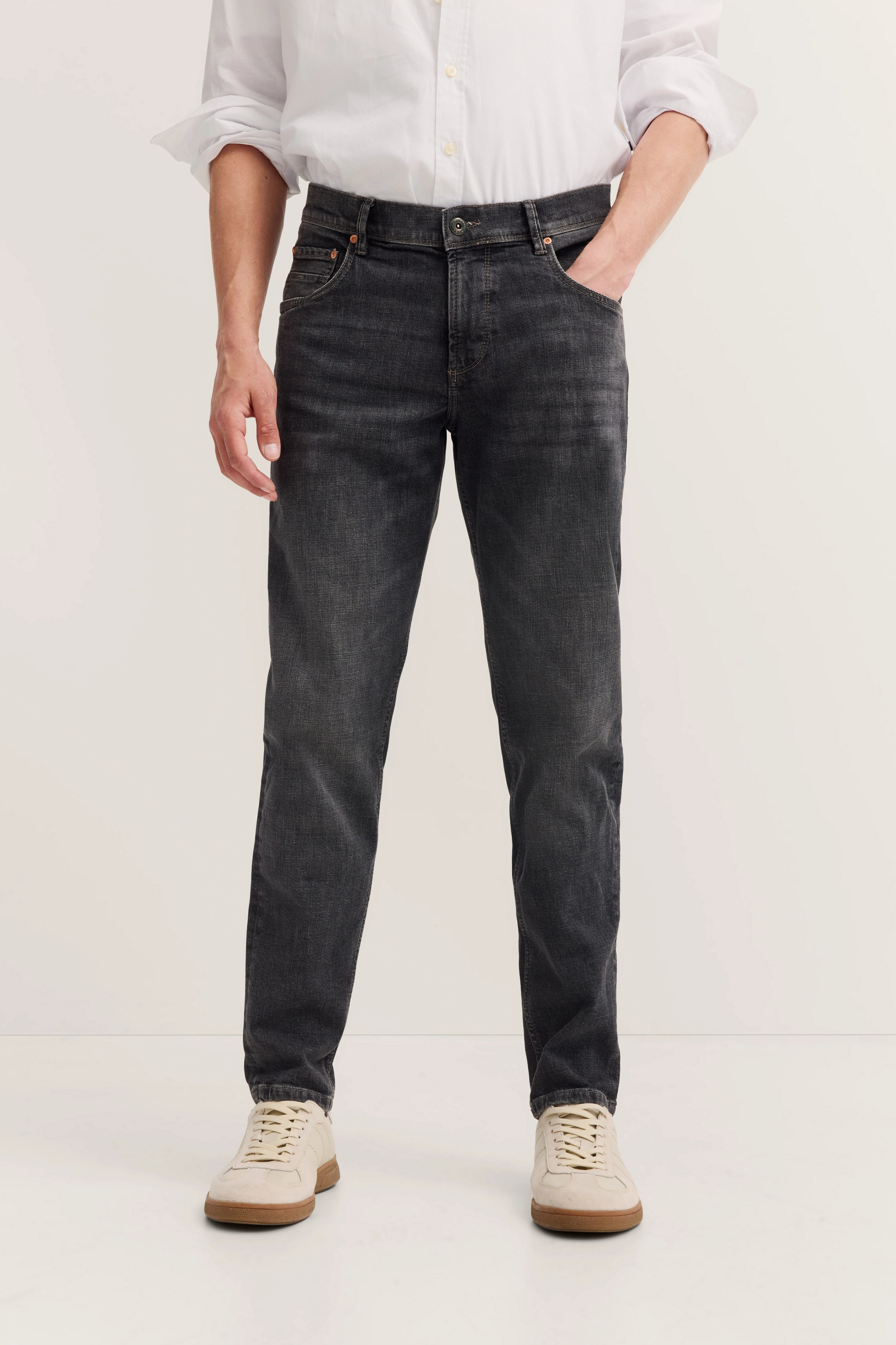 Weiße Hemd und dunkle Jeans mit beigen Sneakers, legeres Modelbild mit entspannter Haltung.