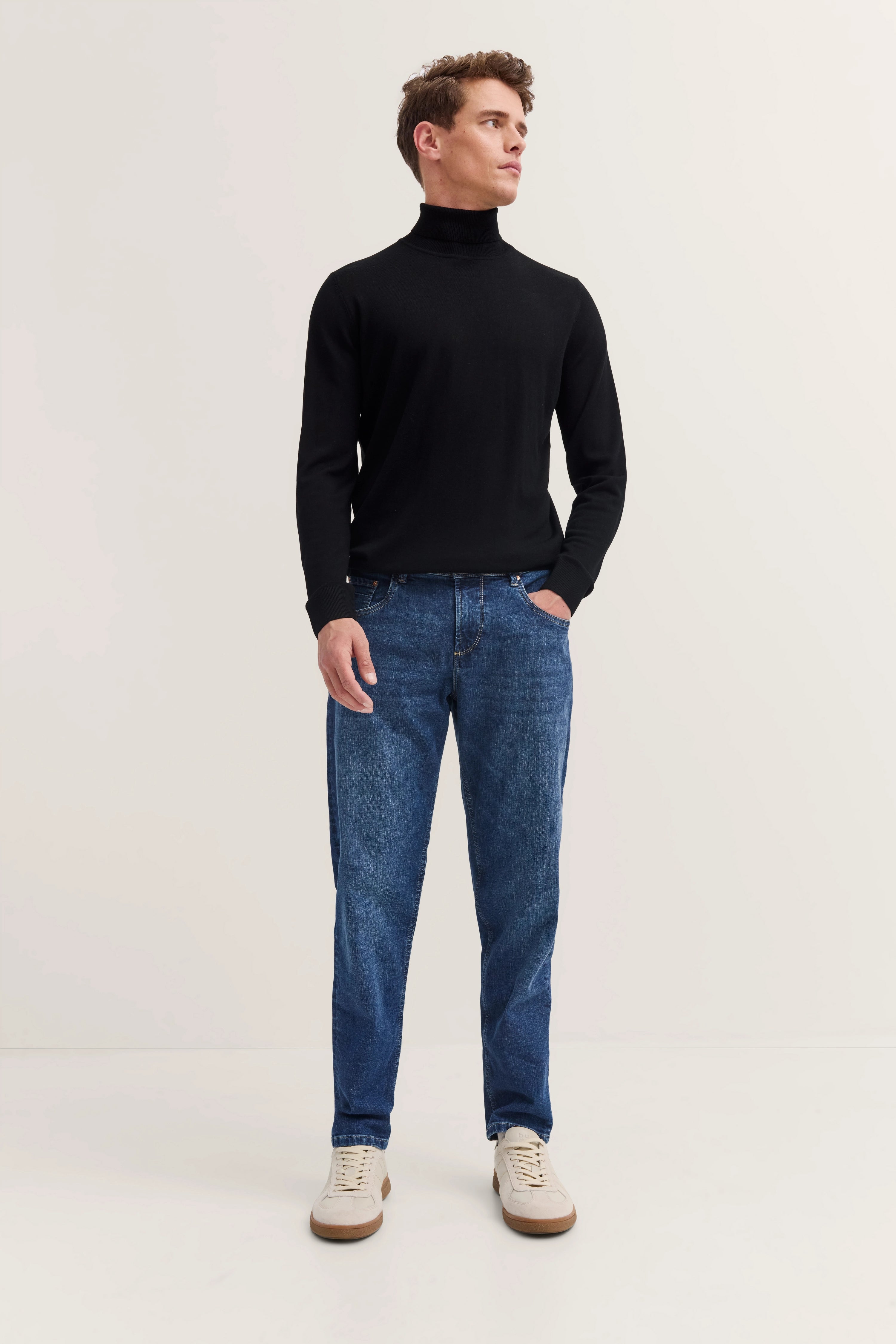 Model in schwarzem Rollkragenpullover, blauer Jeans und weißen Sneakern