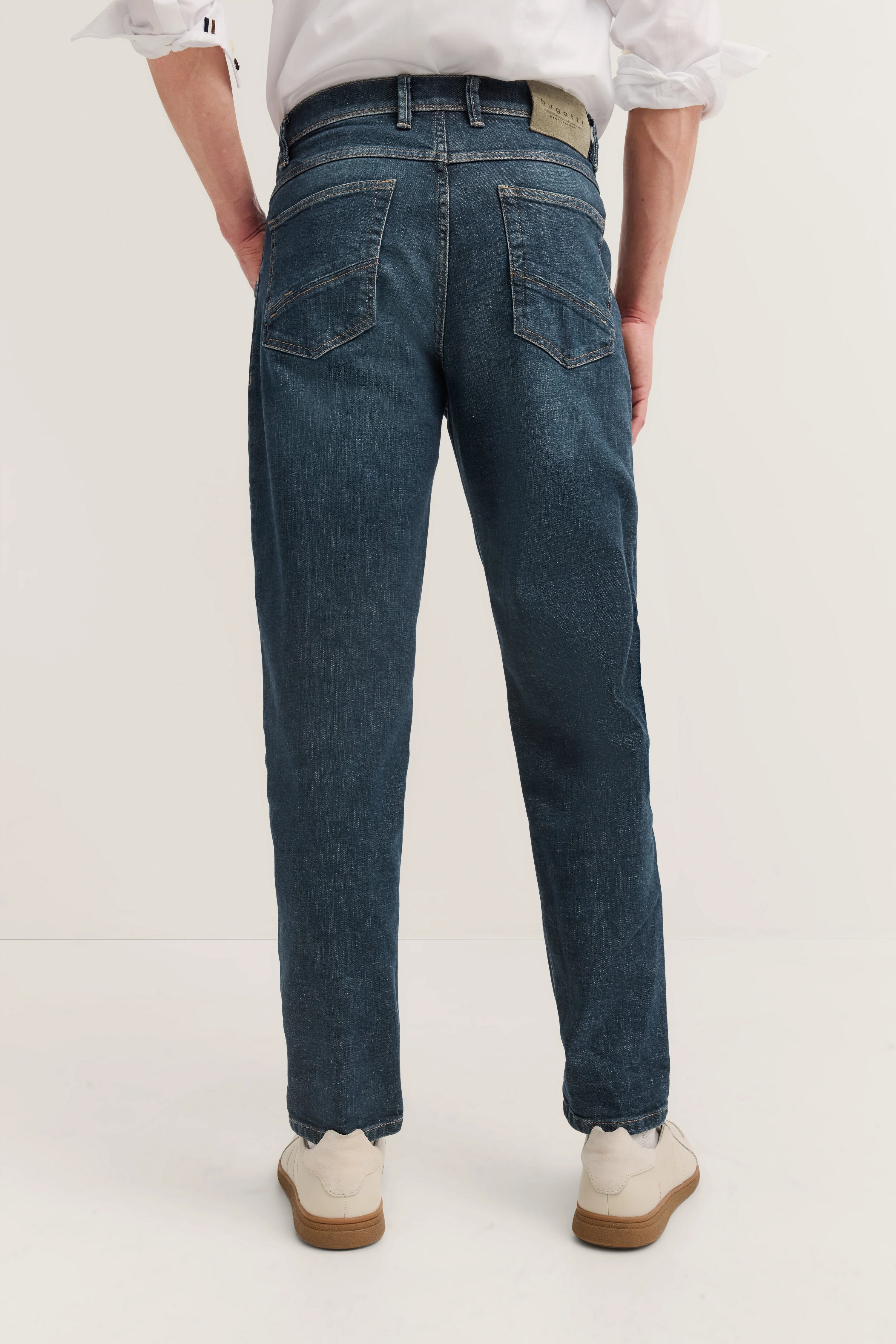 Jeans in Dunkelblau, legeres Modelbild von hinten, weißes Hemd und helle Schuhe.
