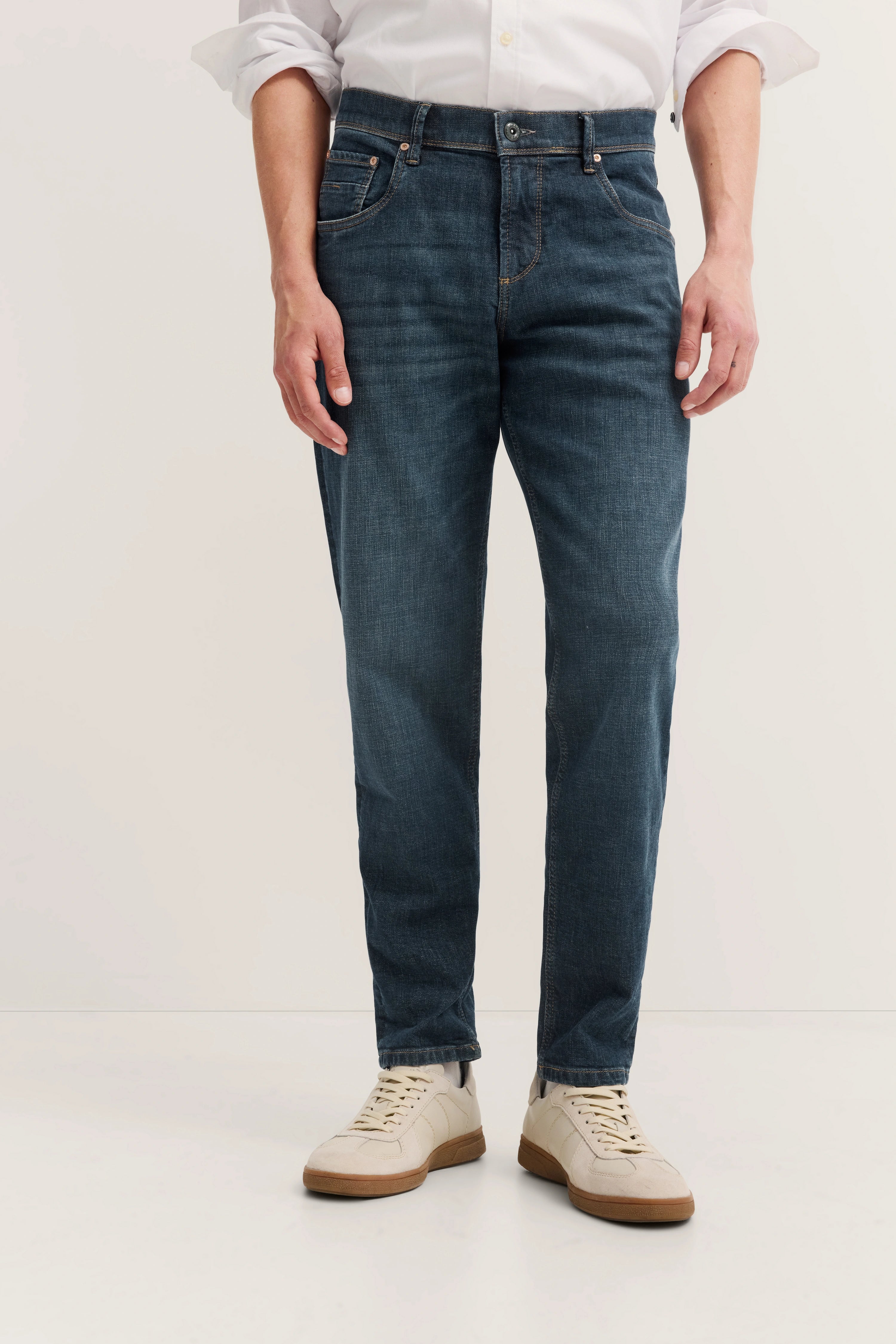 Dunkelblaue bugatti Jeans mit heller Waschung, lässig mit weißem Hemd und Sneakern kombiniert, Modelbild.