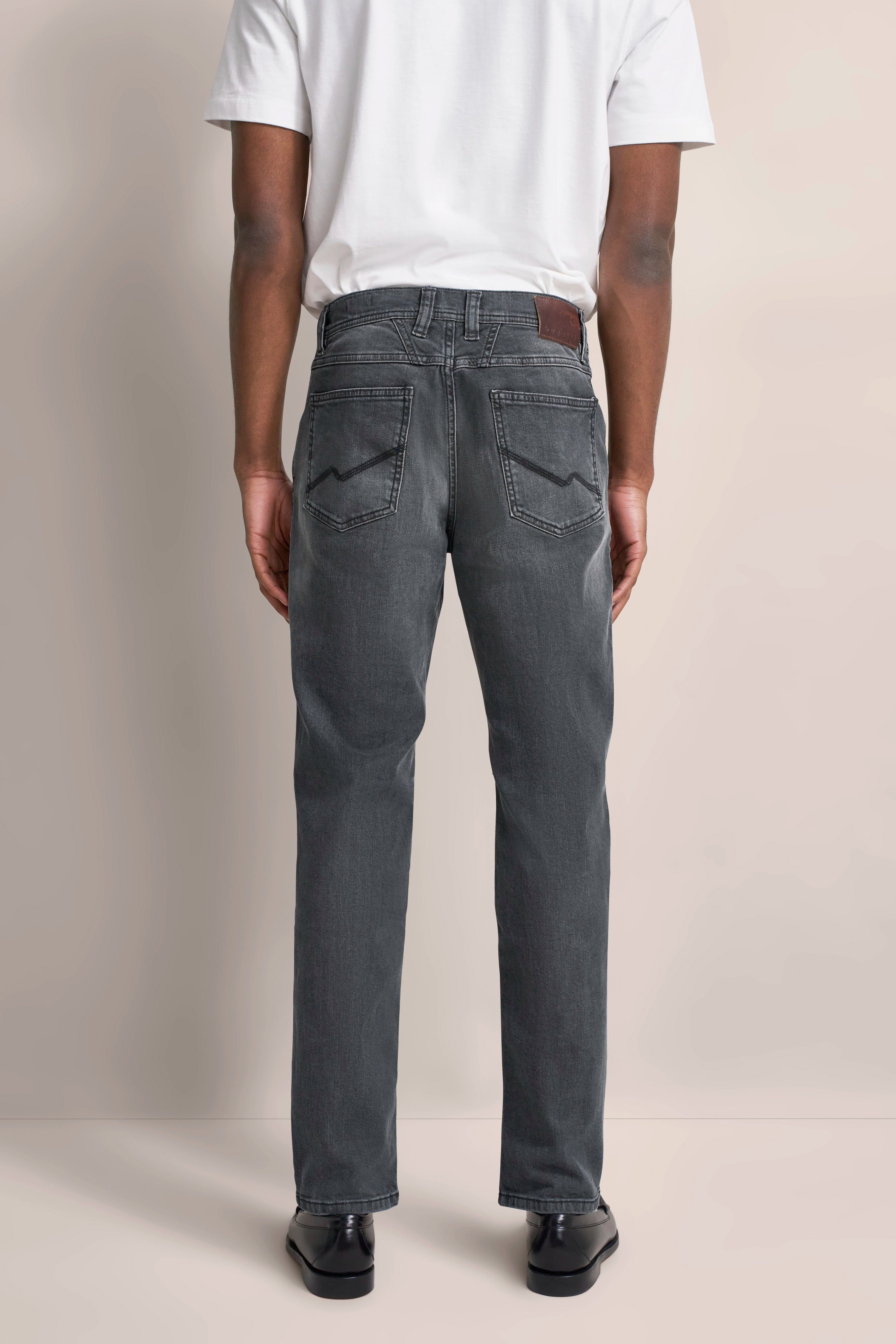 Graue Jeans und weißes T-Shirt, Rückansicht, legeres Modelbild, mit schwarzen Schuhen.