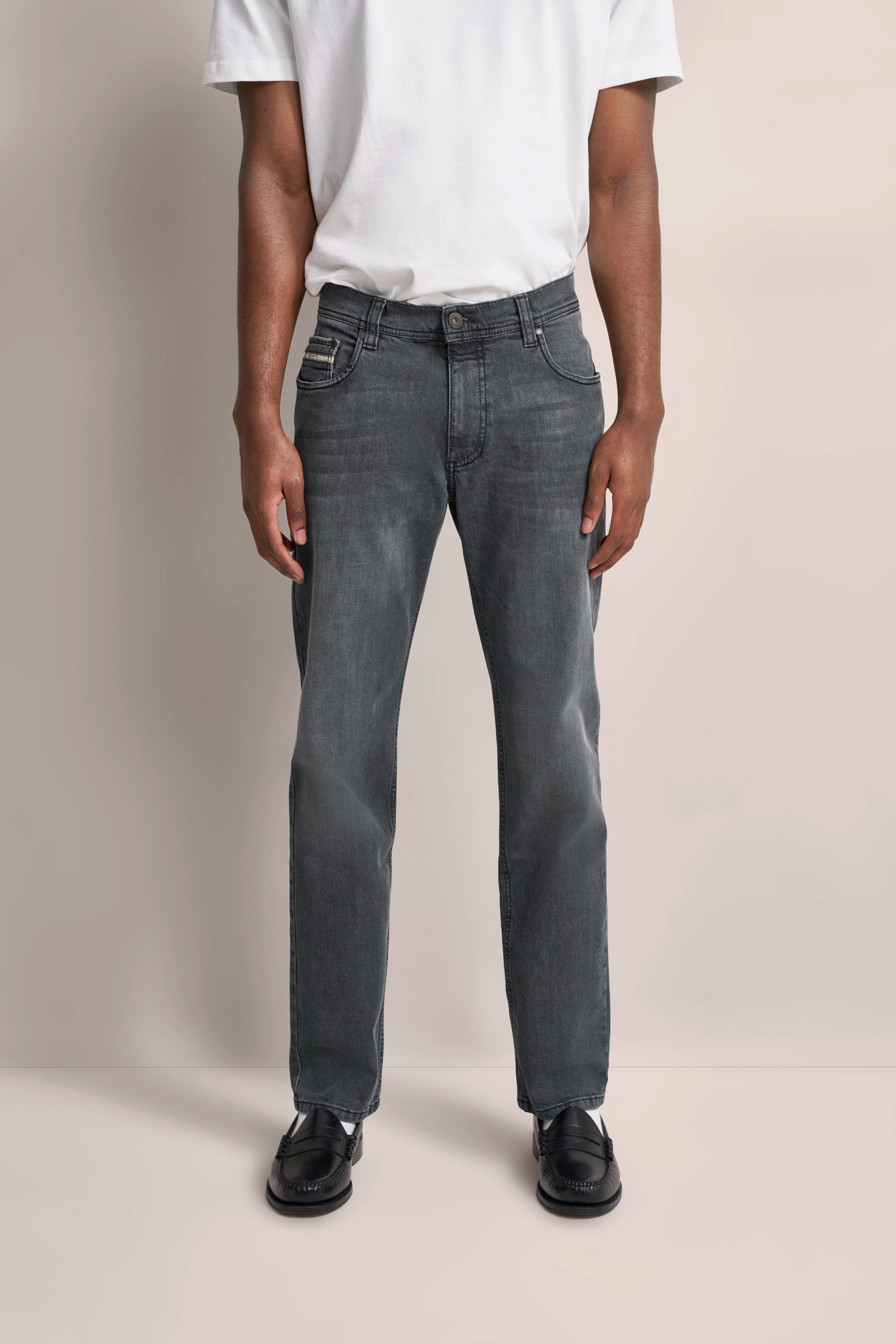 Graue Jeans mit weißem T-Shirt, leger, schwarze Schuhe, Modelbild, entspannte Haltung.