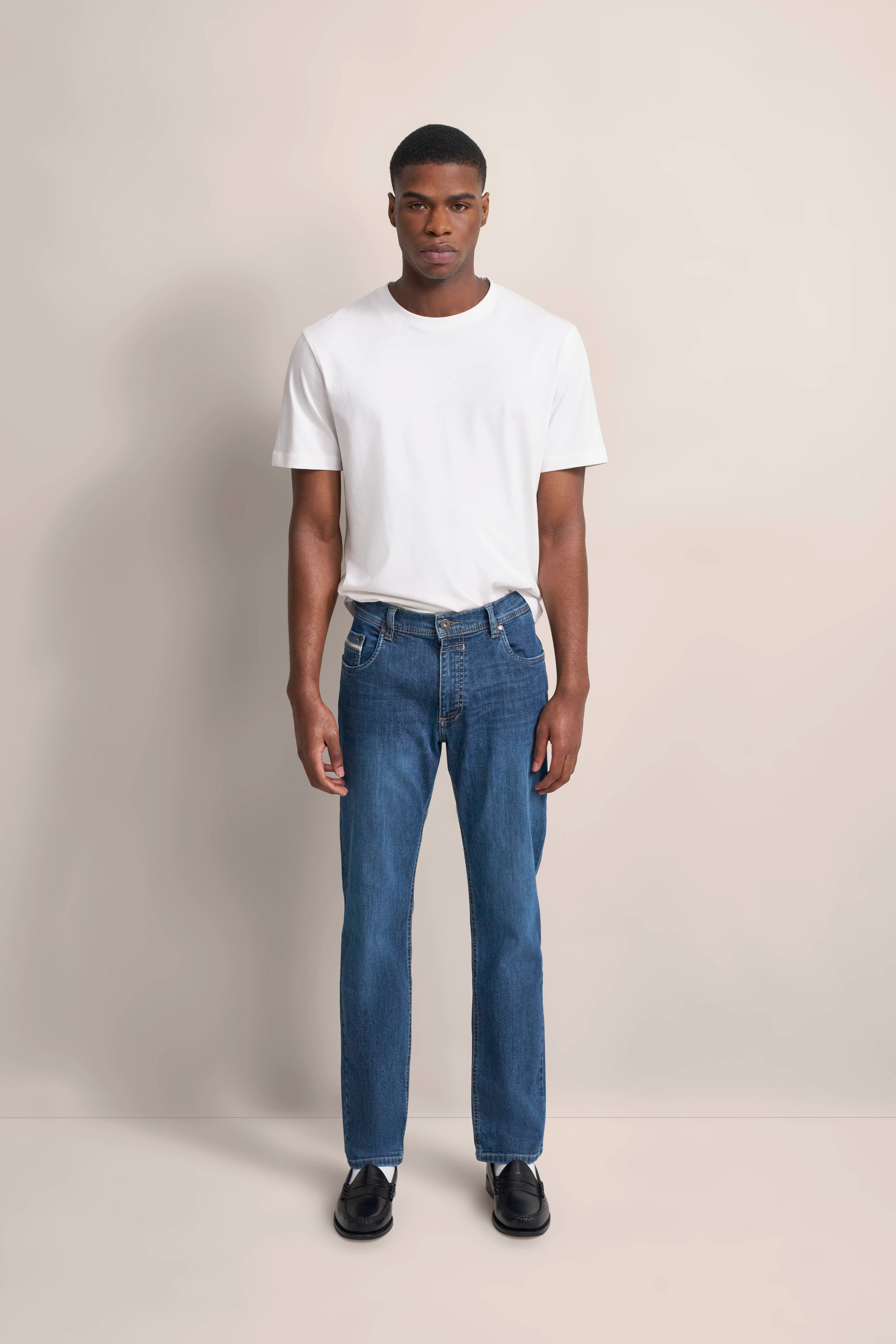 Model in white bugatti T-shirt and blue jeans, standing frontally, wearing black shoes.