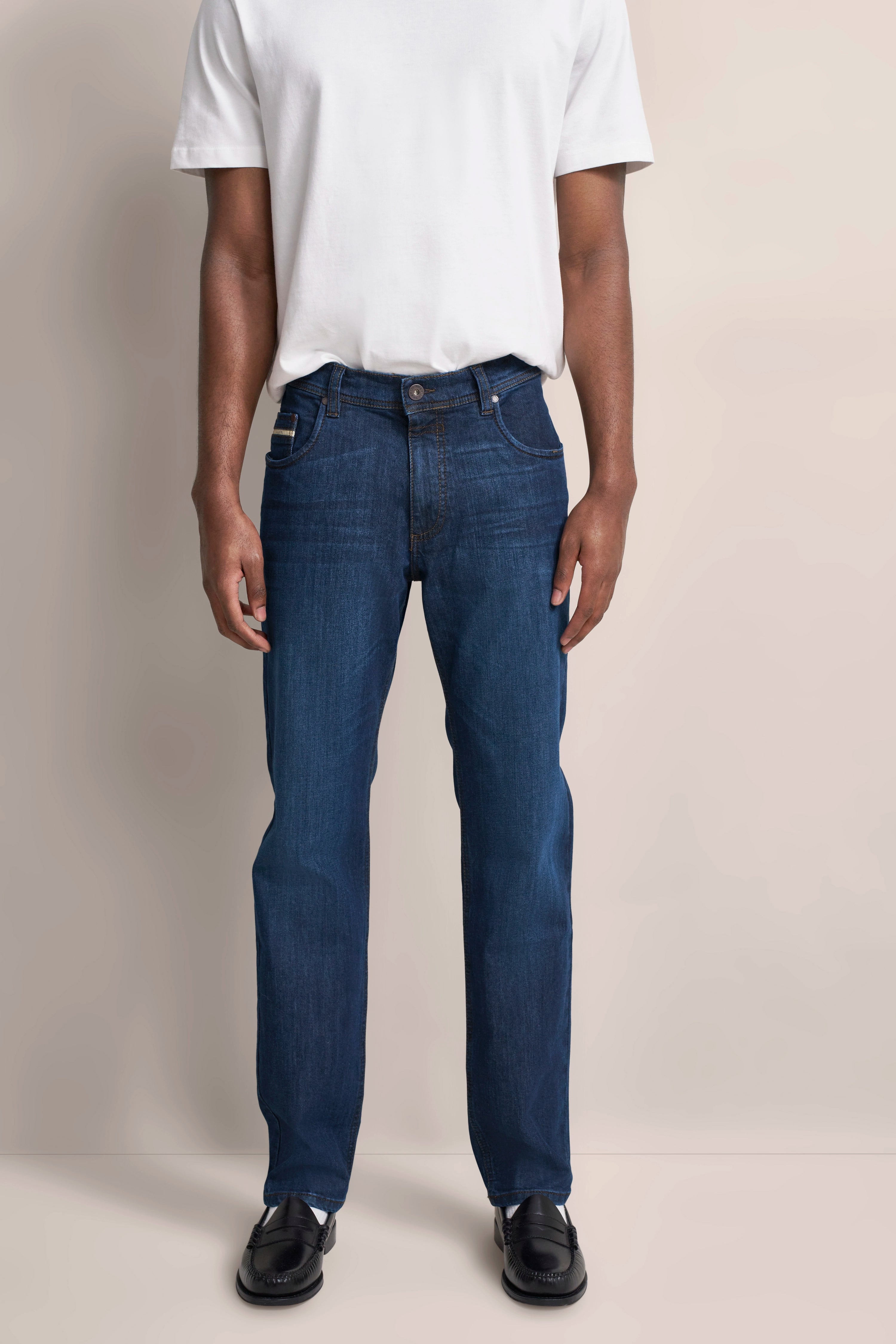 bugatti Jeans in Dunkelblau, legeres Modelbild, weißes T-Shirt, entspannte Pose.