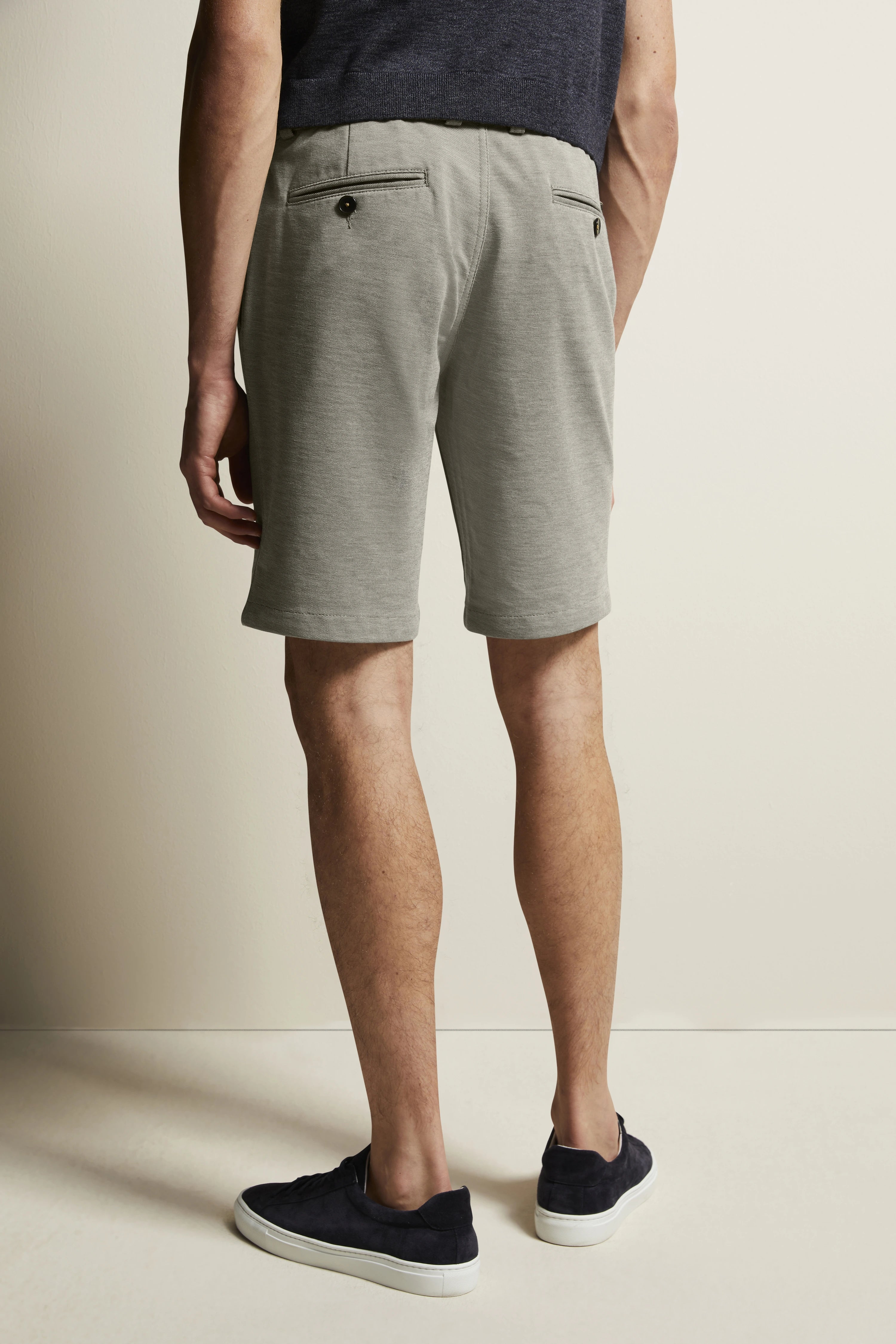 Kurze graue Shorts, dunkles Shirt, lässiger Look von hinten, Modelbild, stehende Pose.