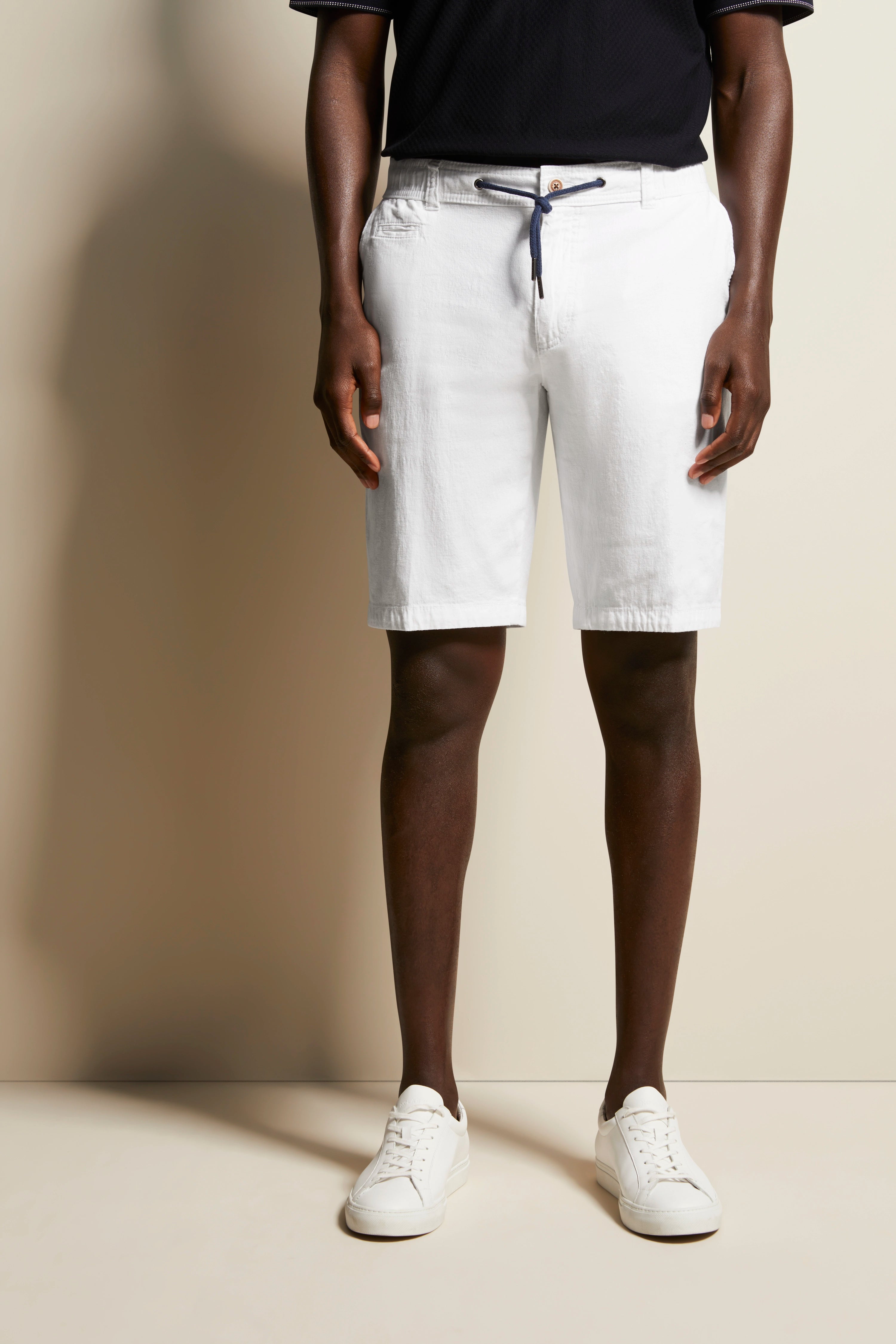 White shorts with belt, black polo, white sneakers, casual model image, relaxed pose.