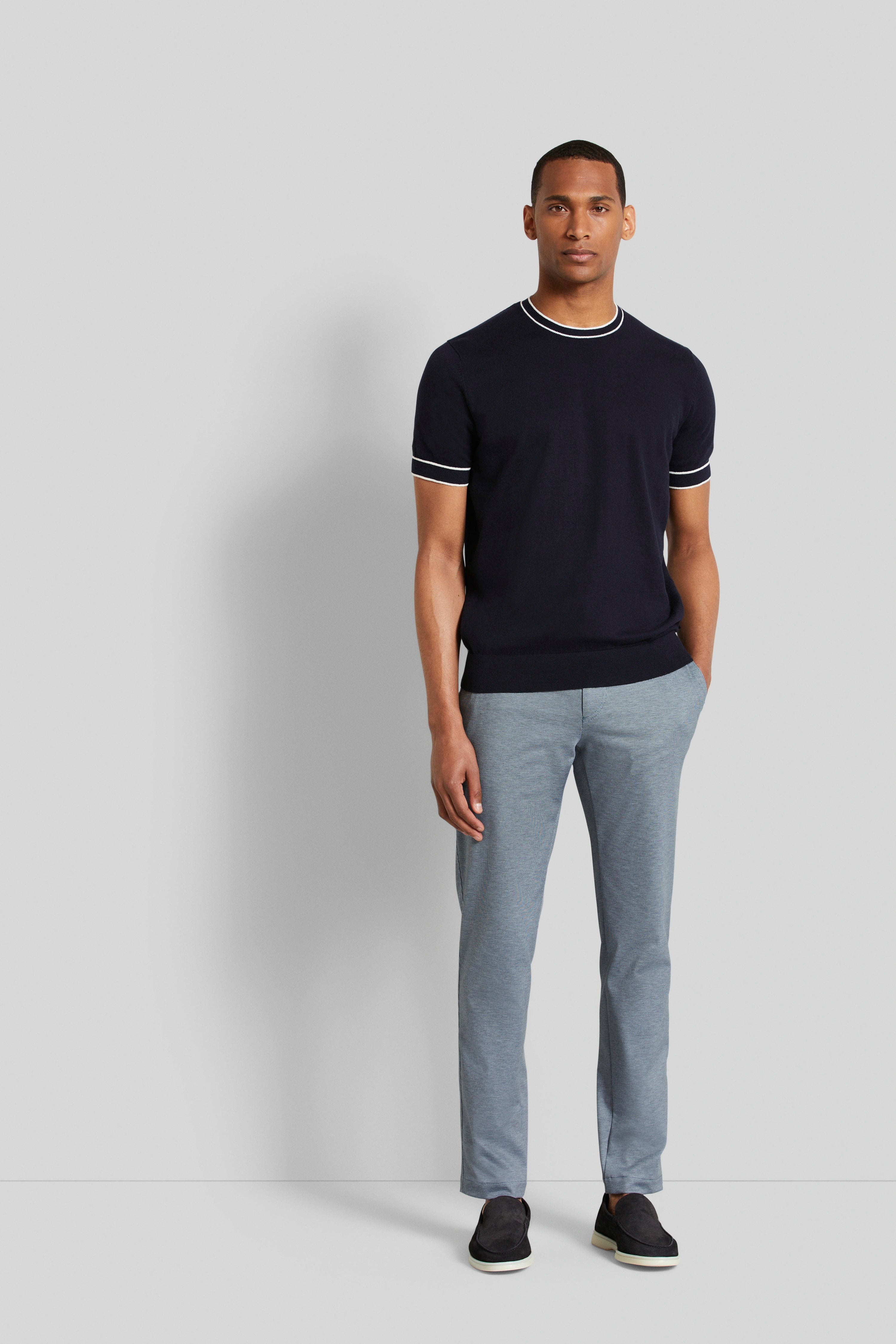 Model in navy bugatti T-shirt and striped gray pants, casual pose, hands in pockets.
