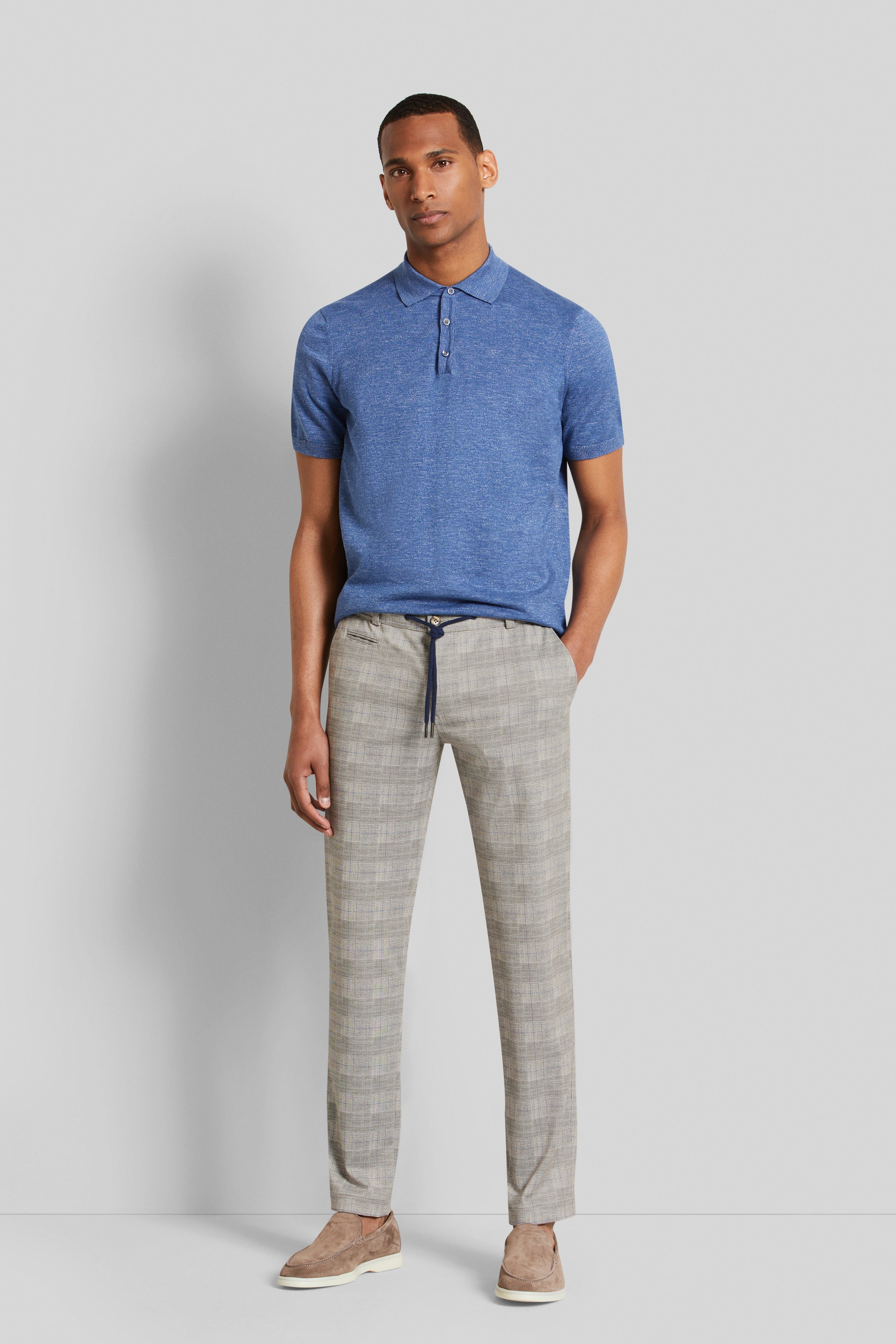 Model in blauw poloshirt en geruite broek, ontspannen pose.