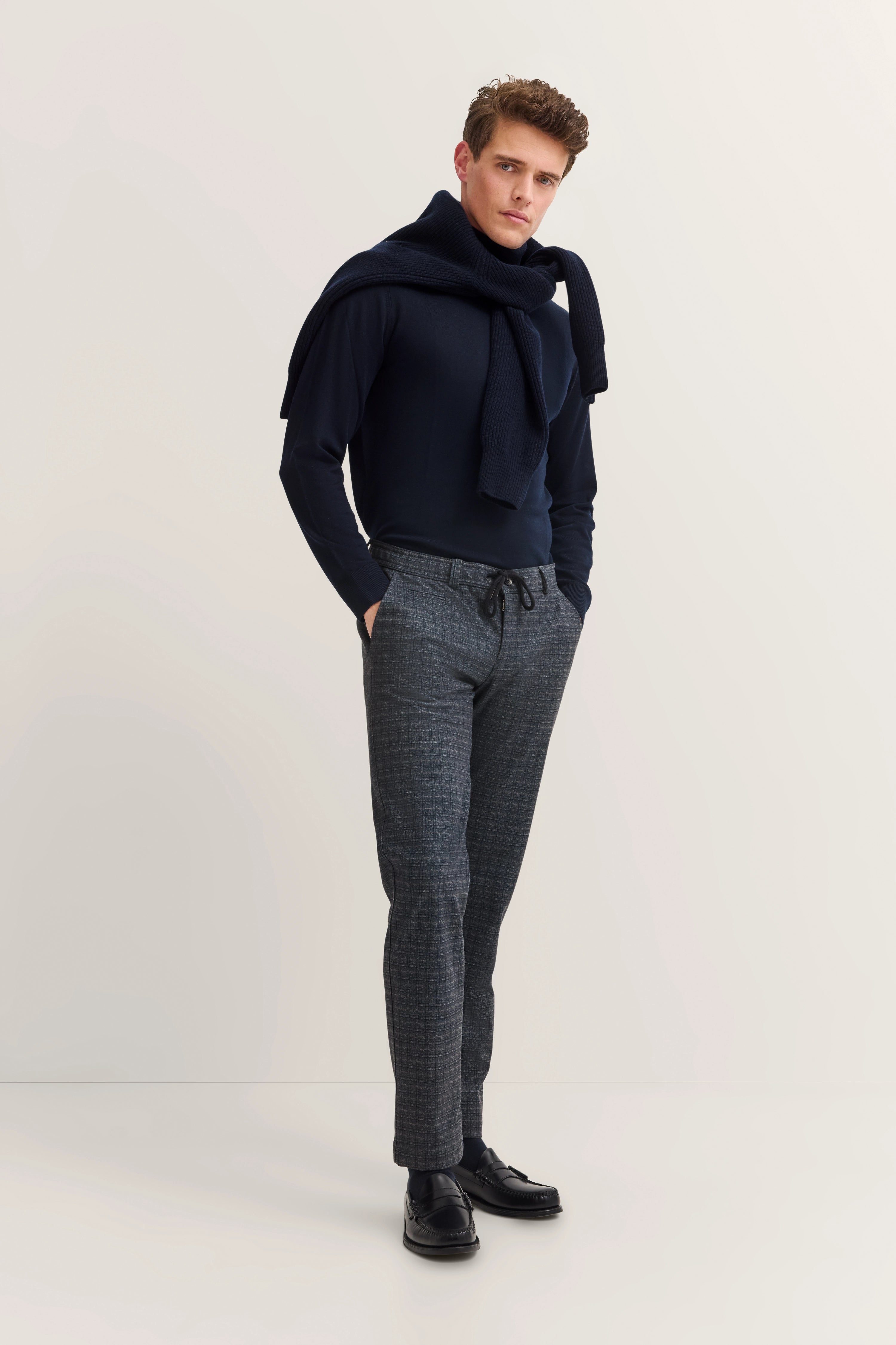 bugatti model in dark blue sweater with scarf, gray pants, casual pose, timeless style.