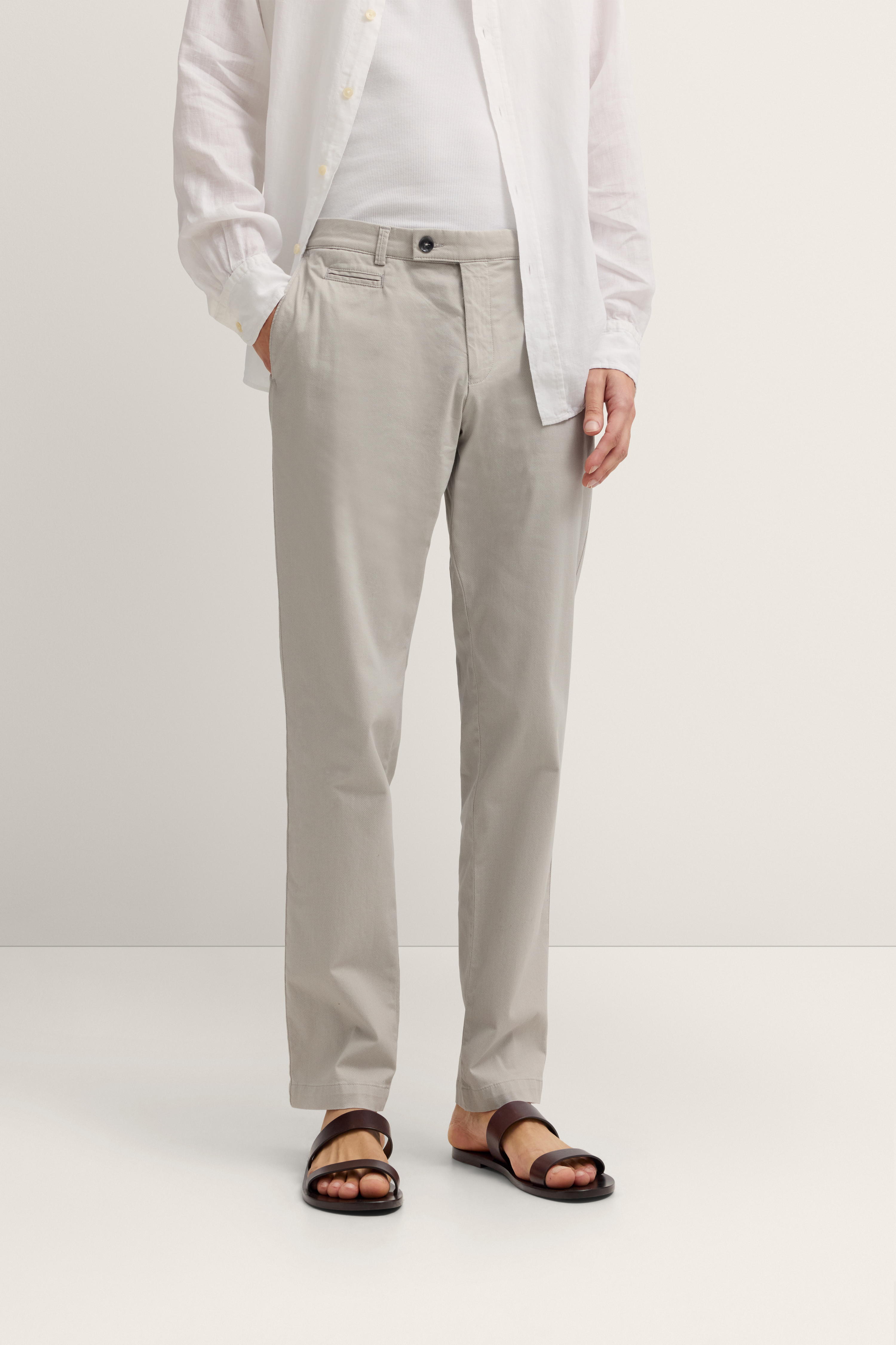 Weißes Hemd, beige Chinos, braune Sandalen, legeres Modelbild, entspannte Pose.