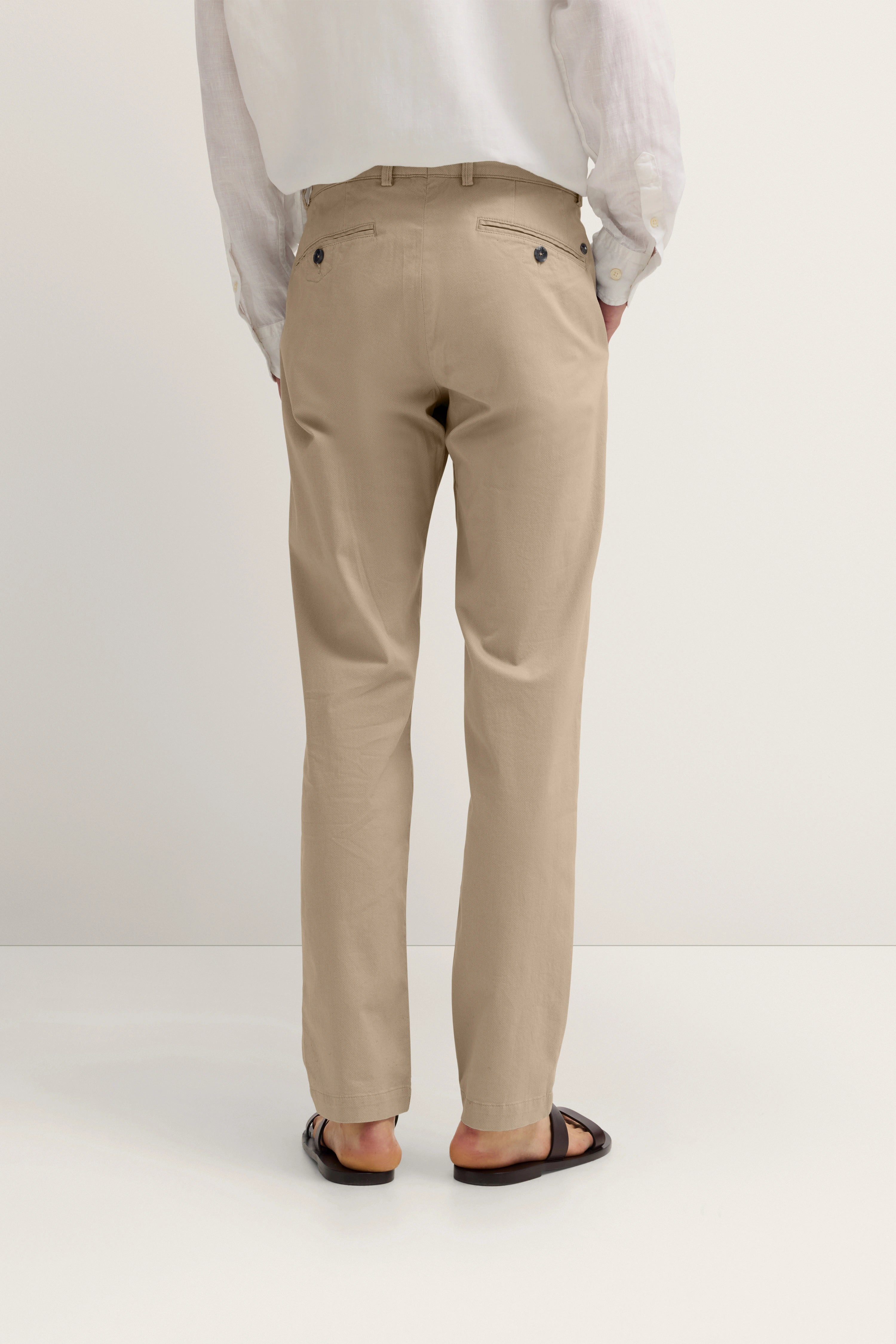Beige Chinos und weißes Hemd von bugatti, legeres Modelbild von hinten, entspannte Pose.