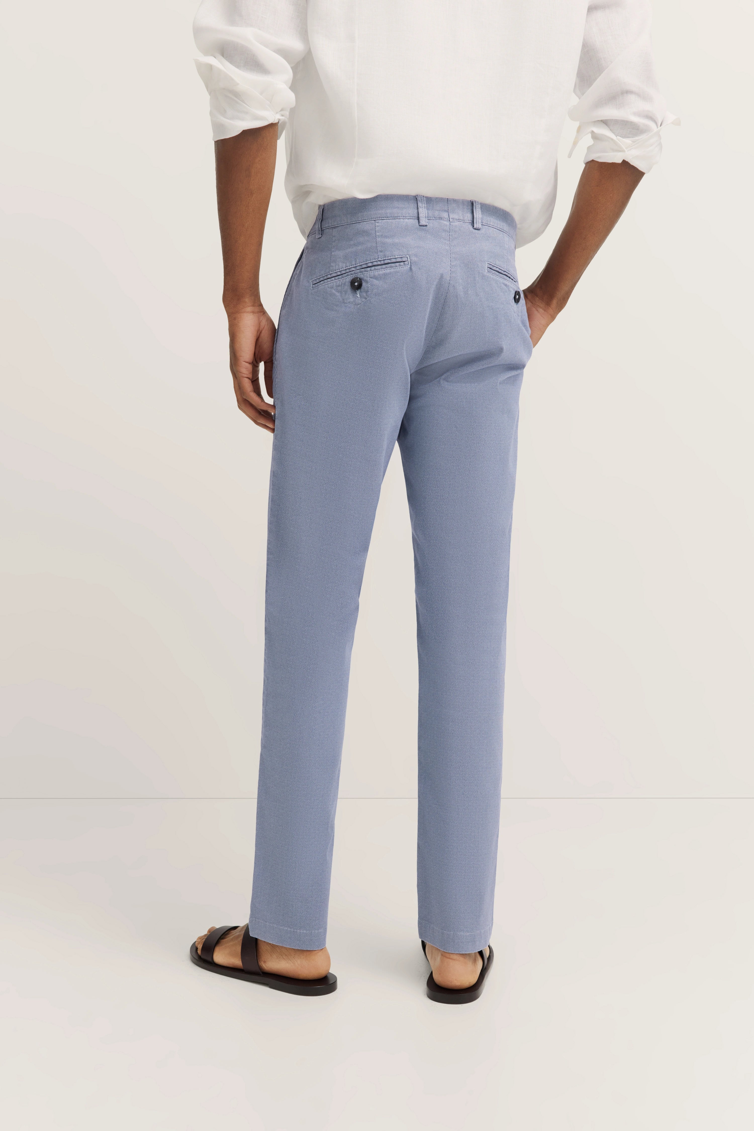 bugatti legeres Modelbild, hellblaue Hose, weißes Hemd, Sandalen, entspannte Haltung.