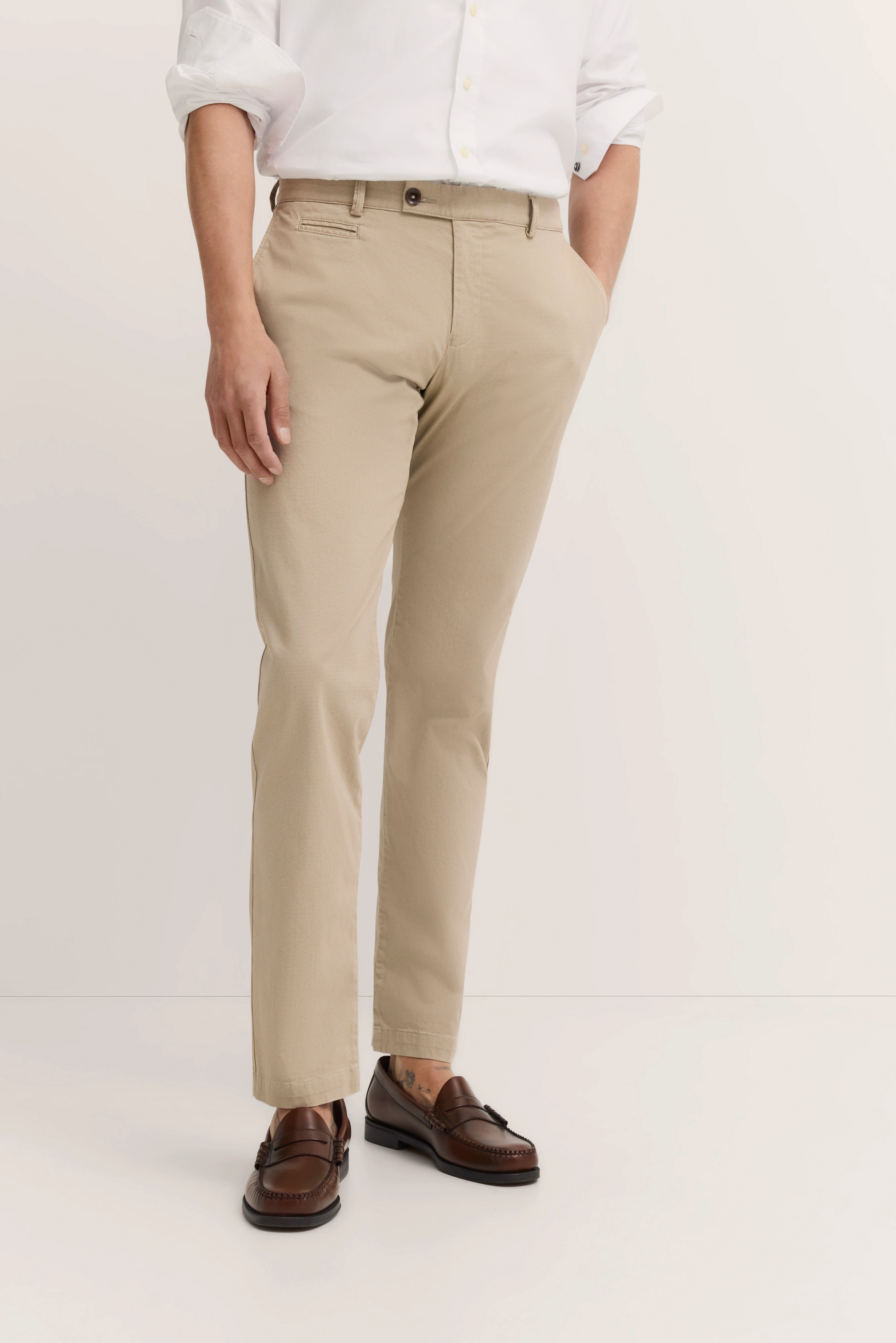 Beige Chinos mit weißem Hemd, braune Loafer. Modelbild, lässige Hand in der Tasche Pose.