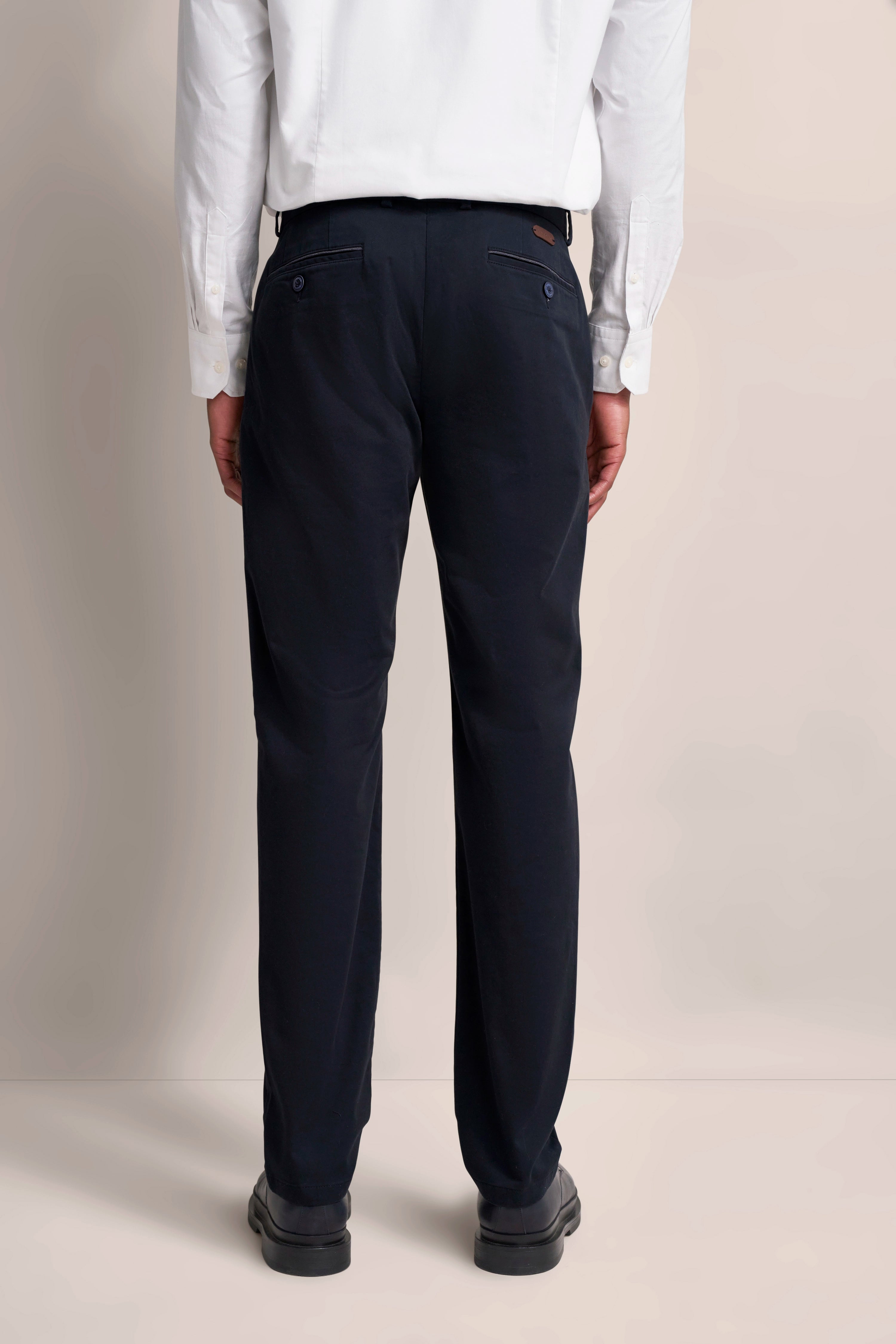 bugatti Modelbild: Weißes Hemd, dunkelblaue Hose, Rückansicht, entspanntes Standposing.